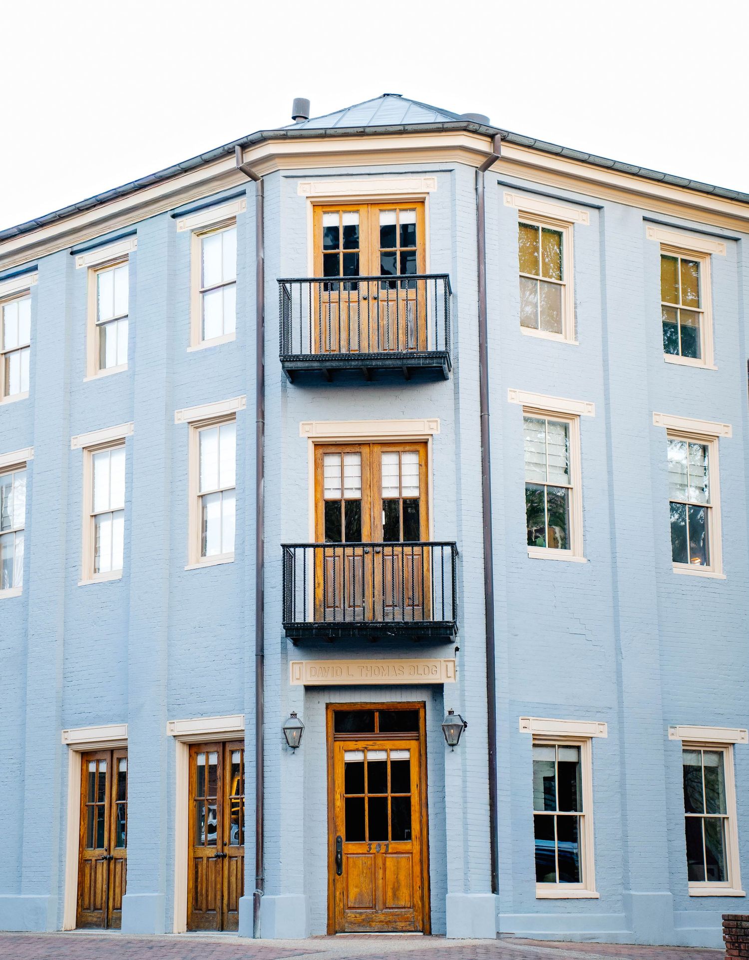 Elegant three-story light blue building with wooden doors and wrought iron balconies in historic district.