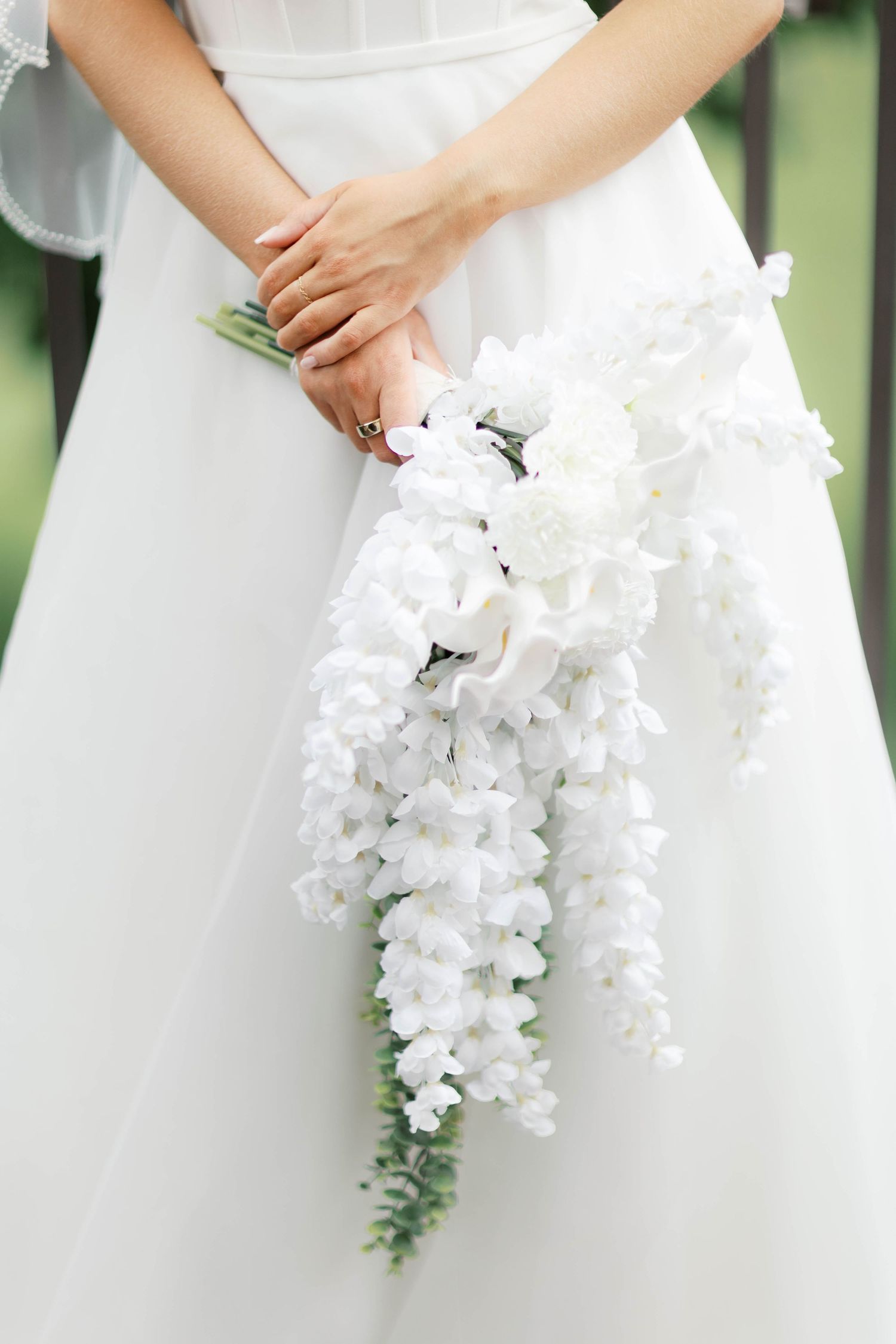 Bride holding an elegant cascading white floral bouquet with delicate wisteria blooms.
