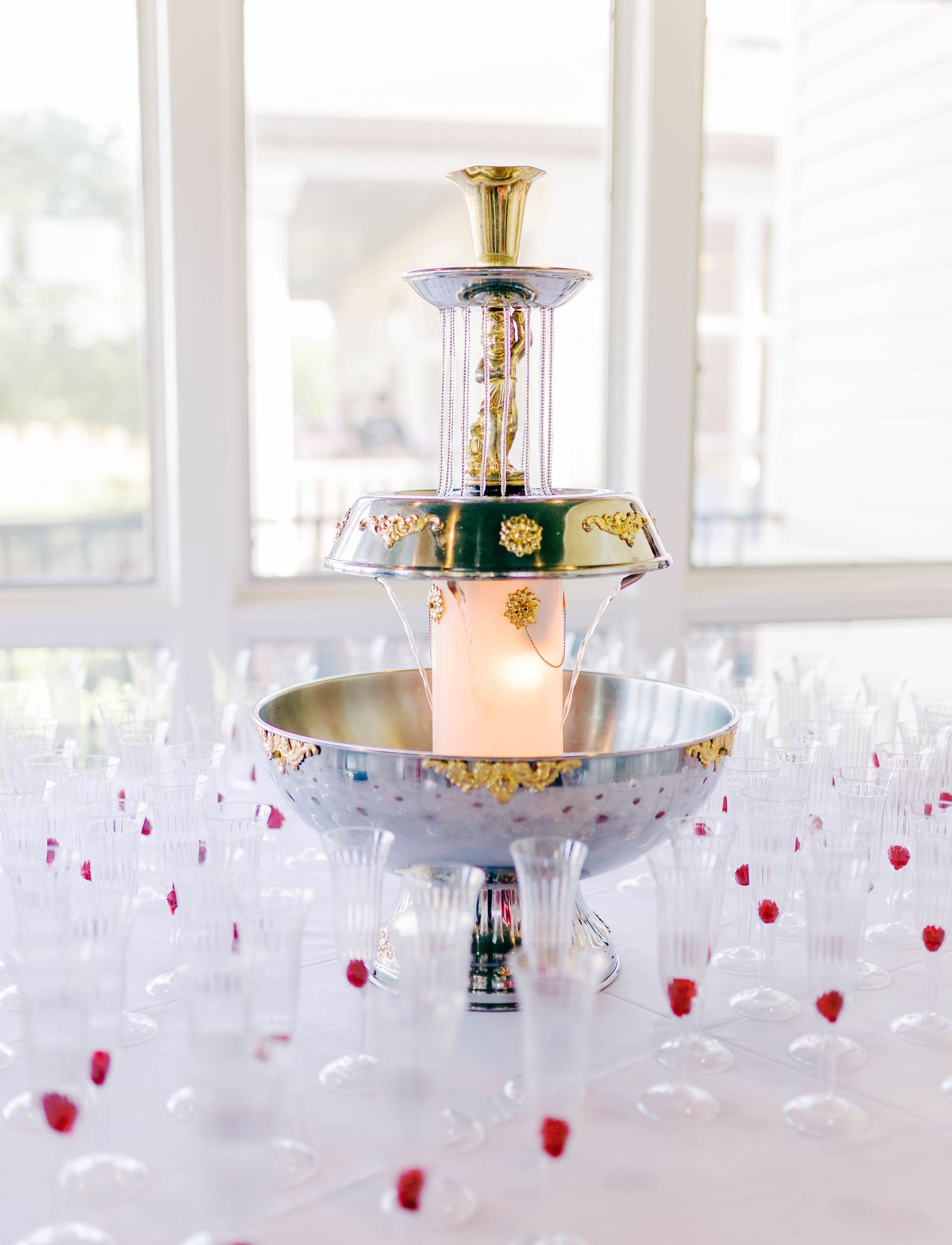 Elegant champagne fountain with gold accents surrounded by crystal glasses and red raspberries at a wedding reception.