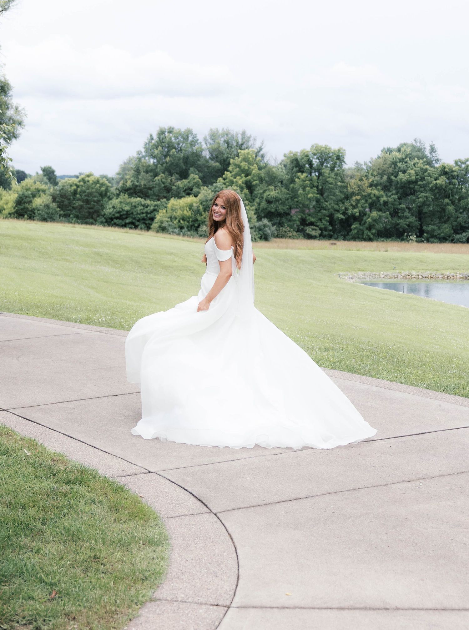 Bride twirls in a flowing white ball gown with veil on a garden path surrounded by lush greenery.
