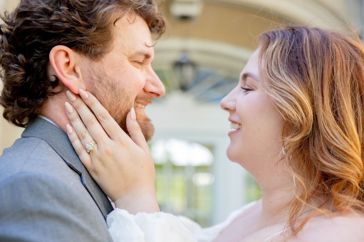 A smiling bride tenderly holds groom's face as they share a romantic moment on their wedding day.