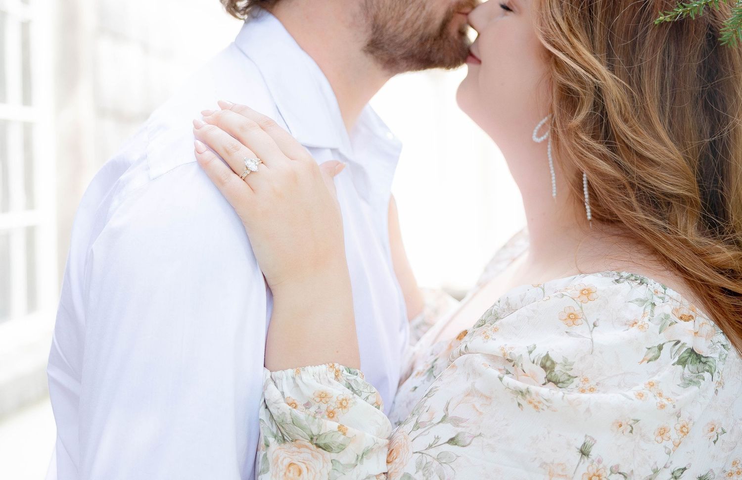 Couple sharing a romantic kiss during engagement photo session, woman wearing floral dress and diamond ring.