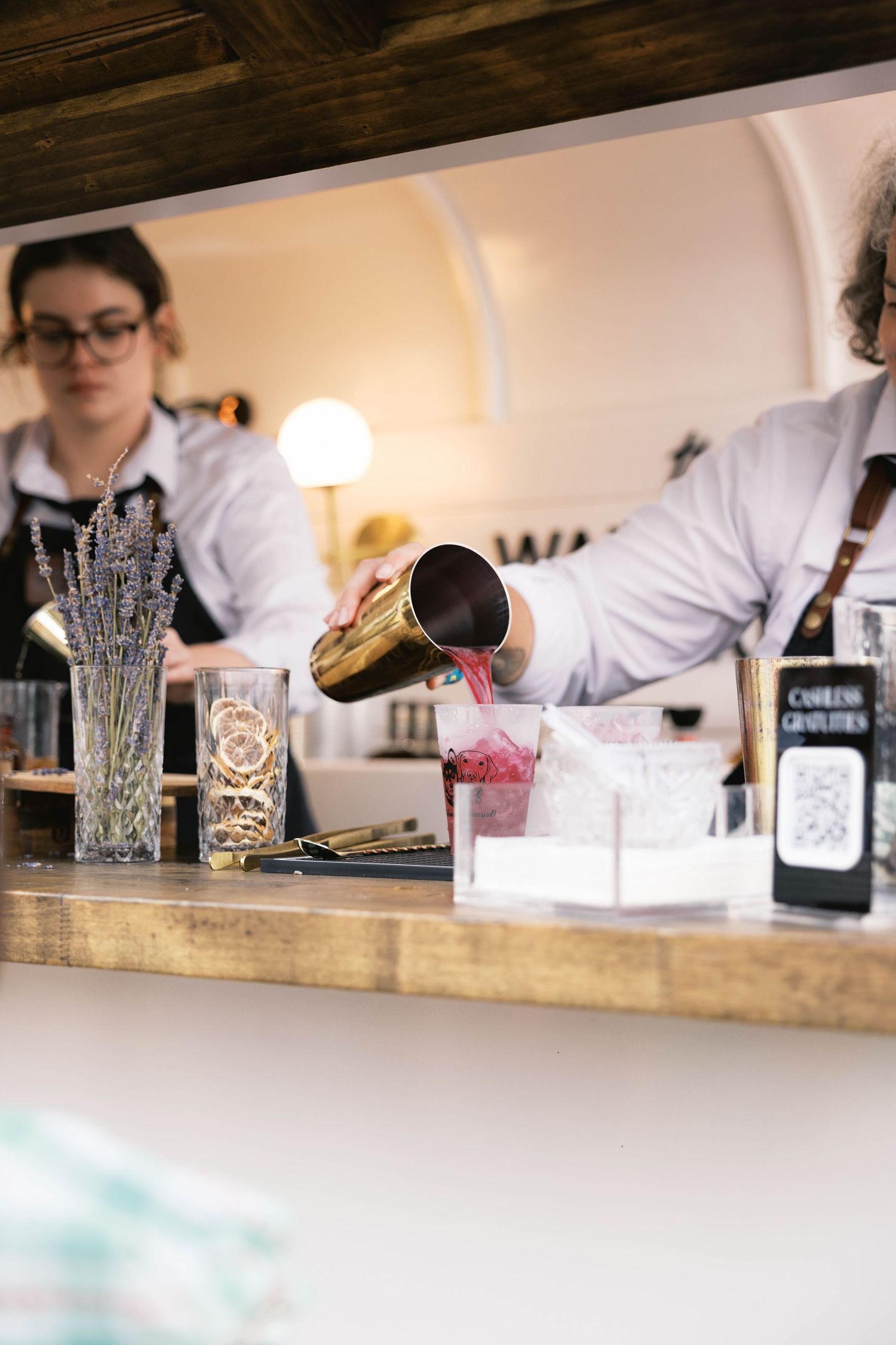 Bartender pouring a pink cocktail from a gold shaker into a glass at a stylish bar counter.