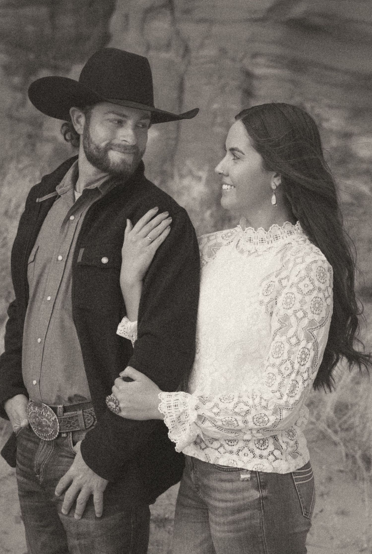 Black and white portrait of couple with man in cowboy hat and woman in lace top outdoors.