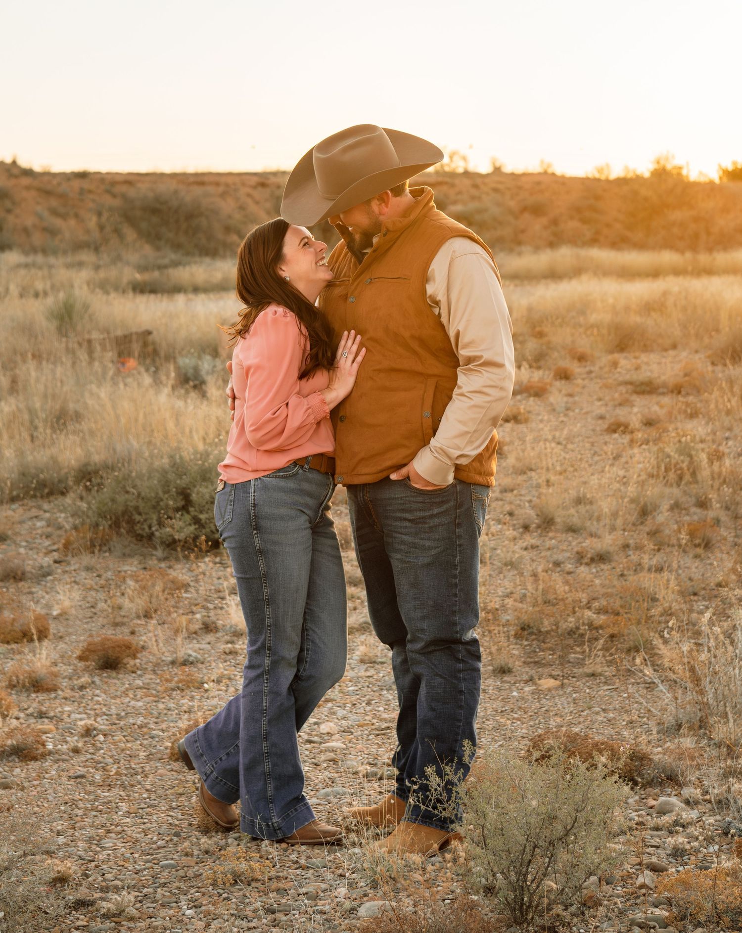 Couple sharing a romantic moment at golden hour in a desert landscape, man wearing cowboy hat.