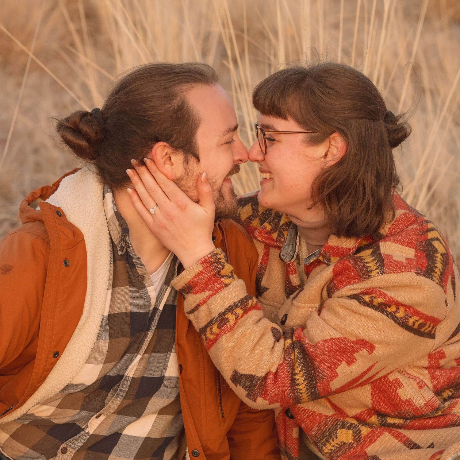 Couple sharing a romantic nose-to-nose moment in a golden field wearing warm autumn jackets.