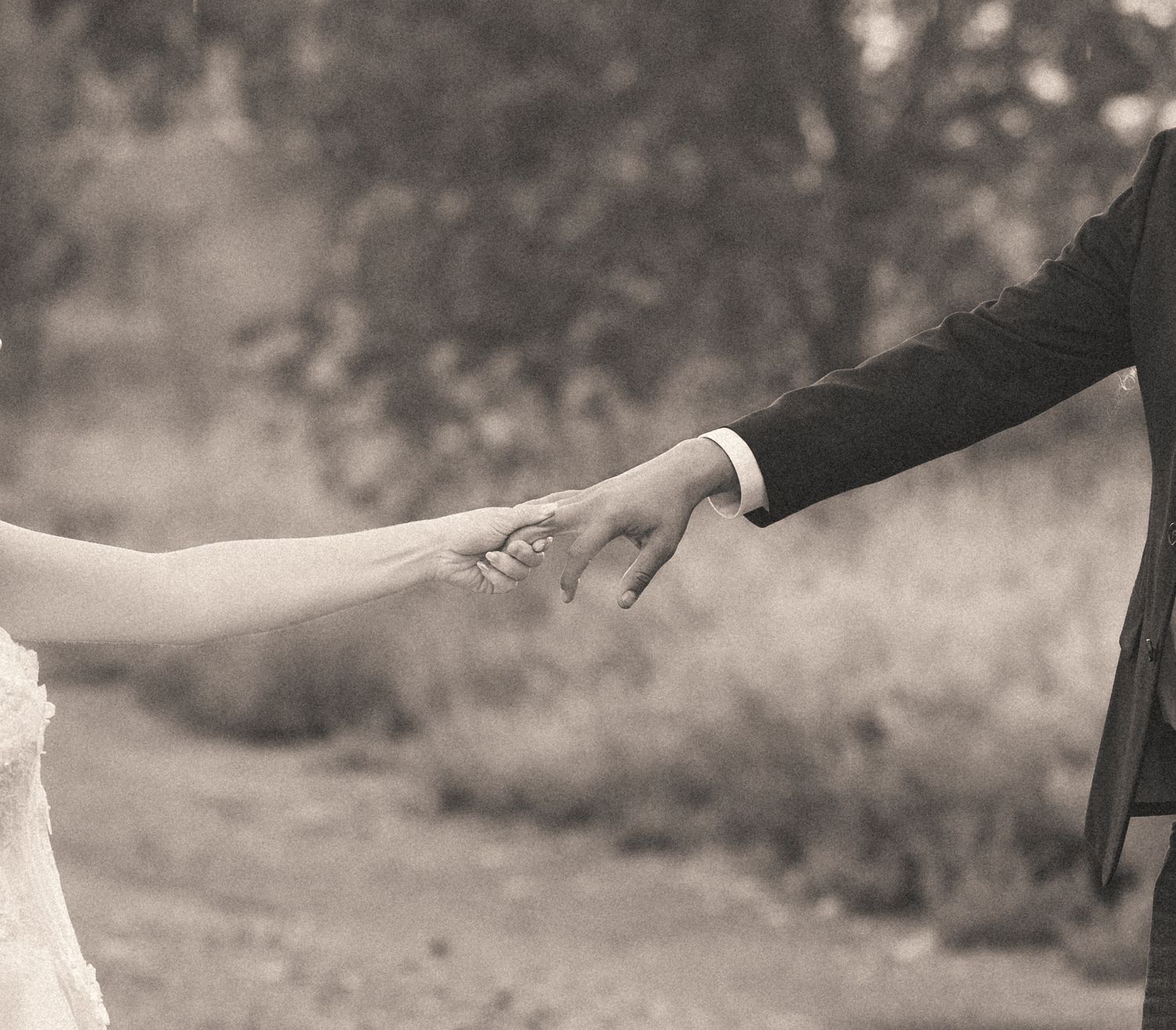 Black and white close-up of bride and groom holding hands outdoors on wedding day.