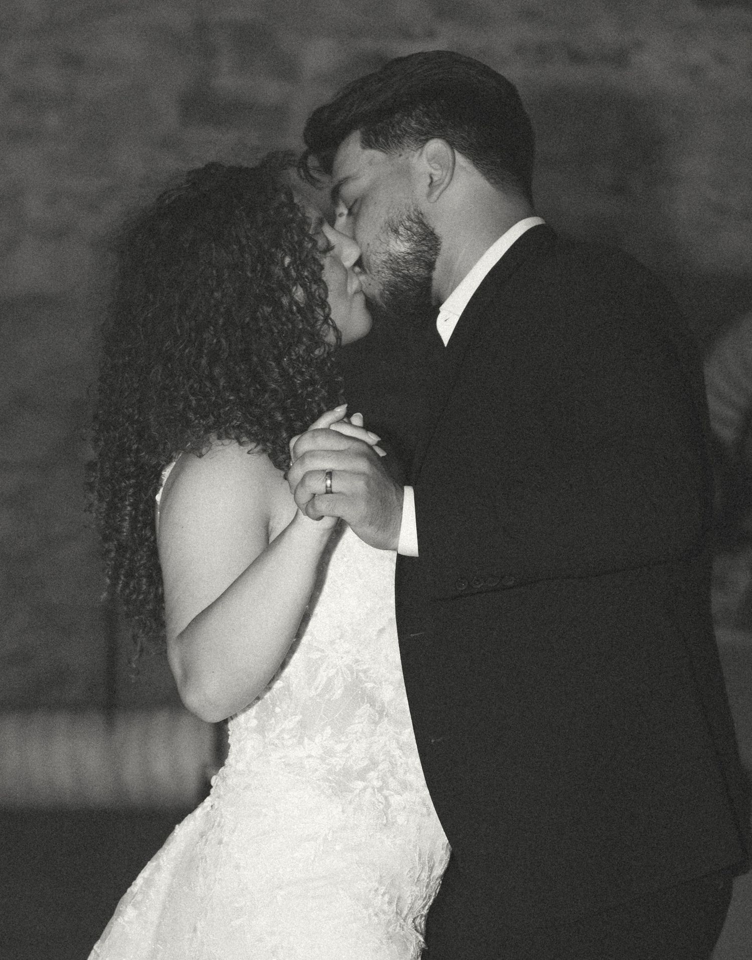 Newlyweds share a romantic kiss during their first dance in black and white.