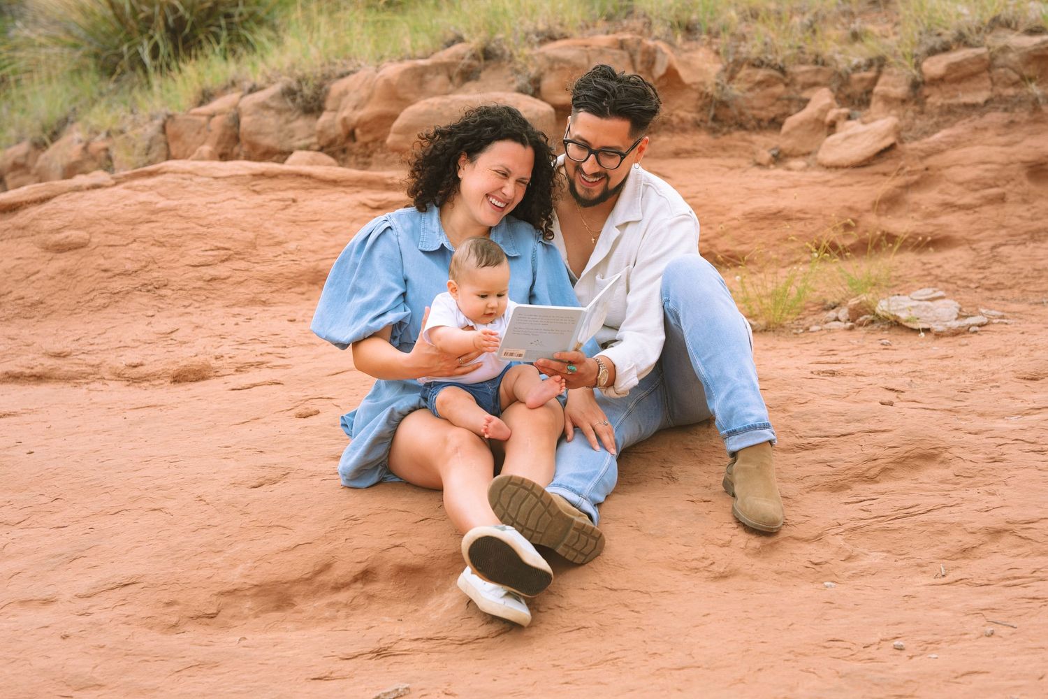 Happy family with baby enjoying a book on red rock.