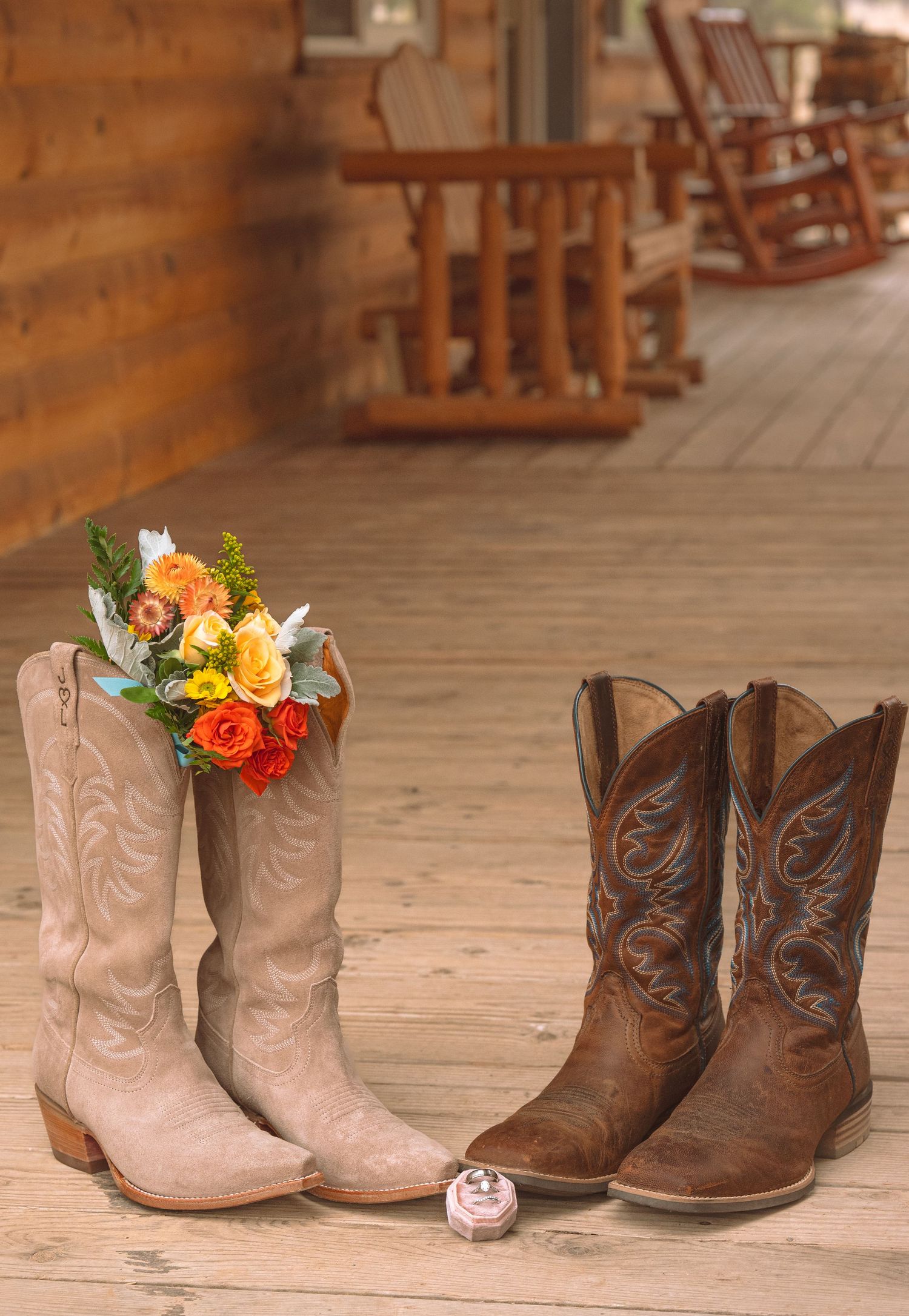 Pair of cowboy boots with colorful floral bouquet and ring on rustic wooden porch.