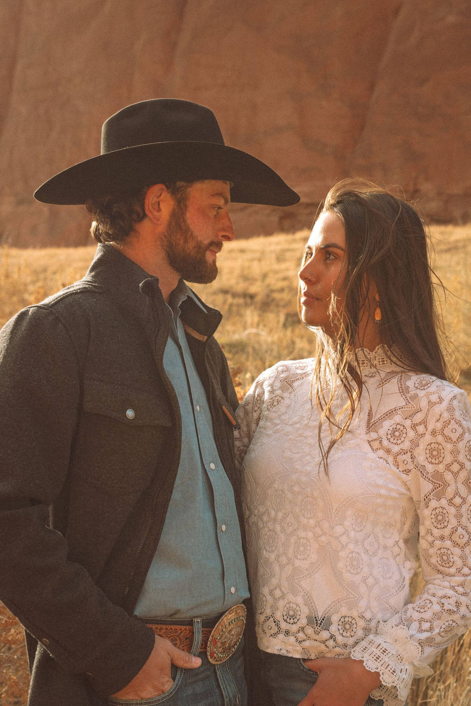Couple in western attire sharing an intimate moment at golden hour with red rock formations behind them.