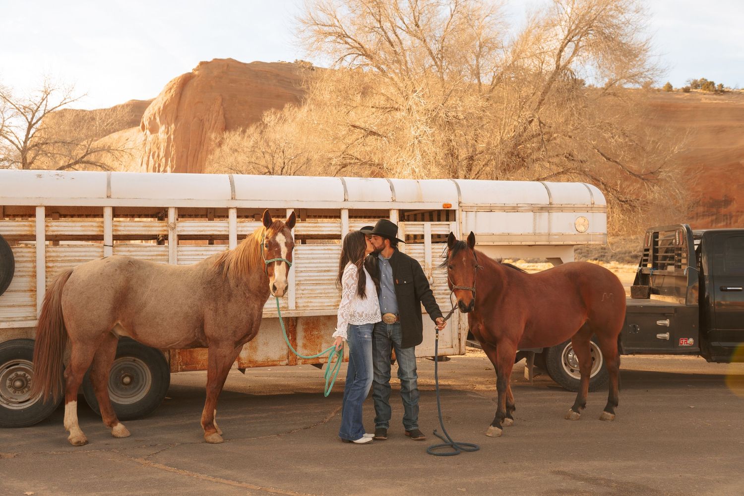 Couple standing with two horses near a trailer with red rock canyon in the background.
