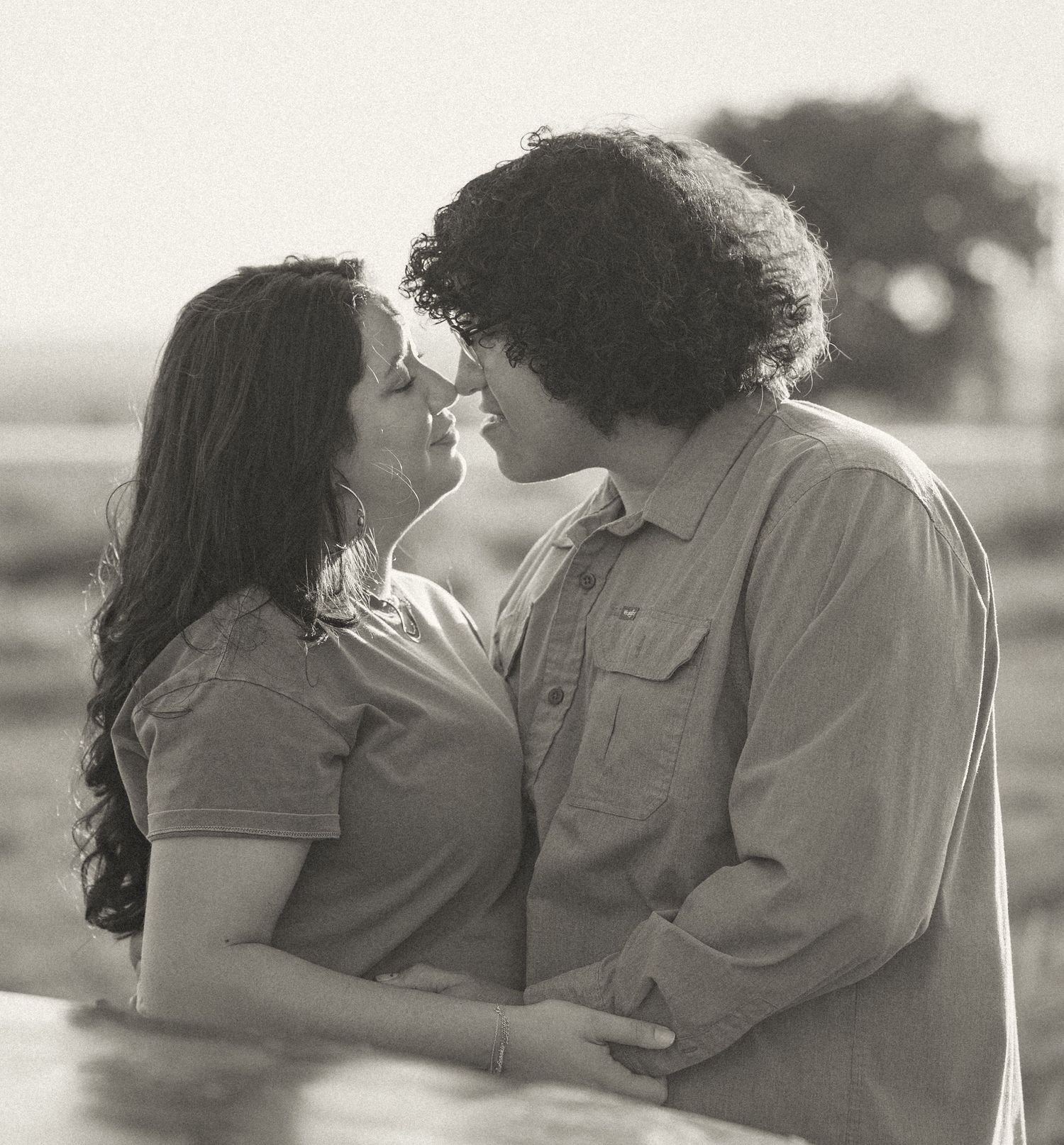 Black and white romantic portrait of couple nearly kissing outdoors in soft natural light.