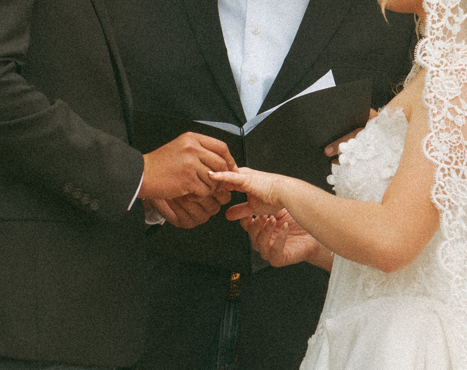 Close-up of groom placing wedding ring on bride's finger during wedding ceremony ring exchange.