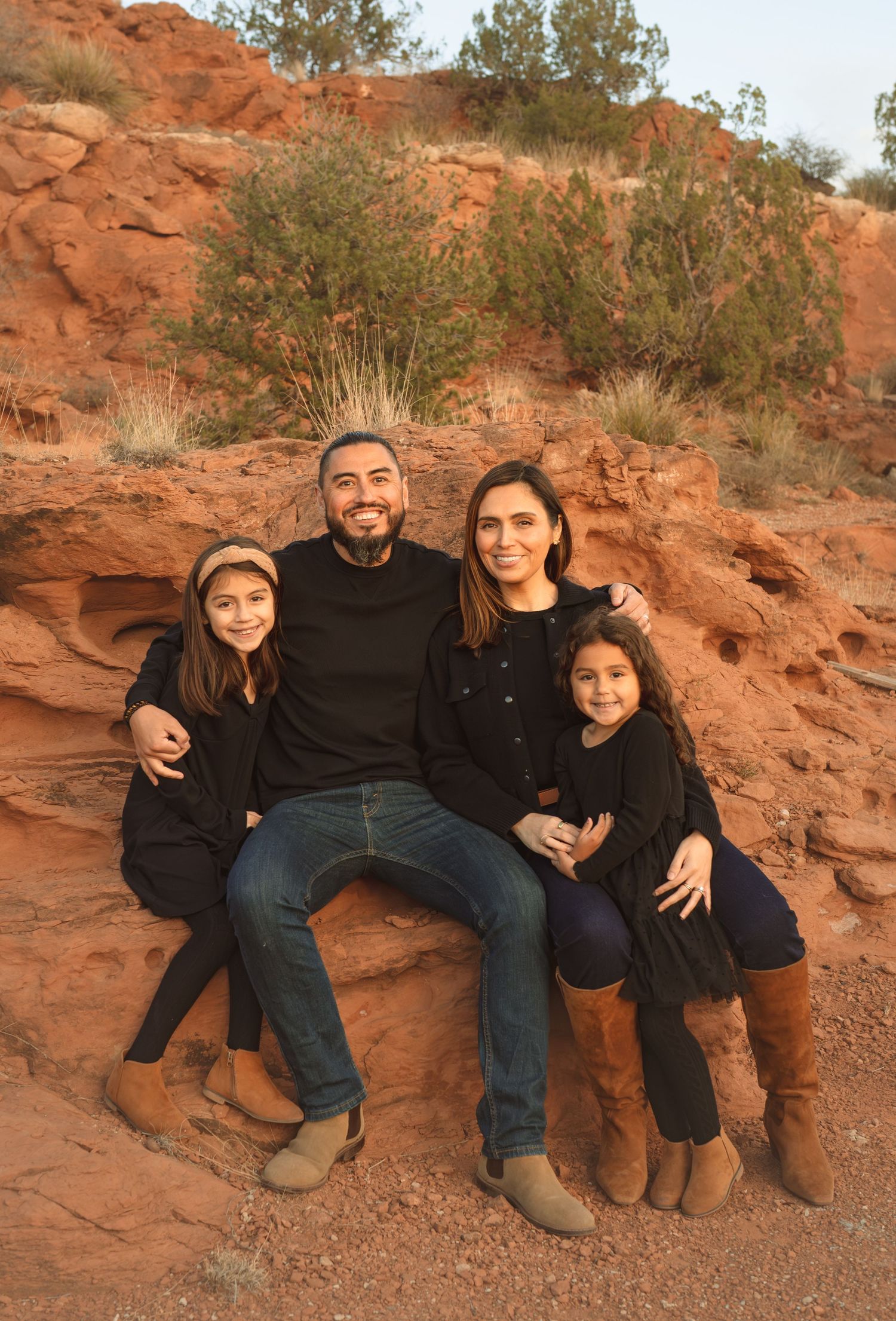 Family of four in matching black outfits posing on red rock formations at sunset.