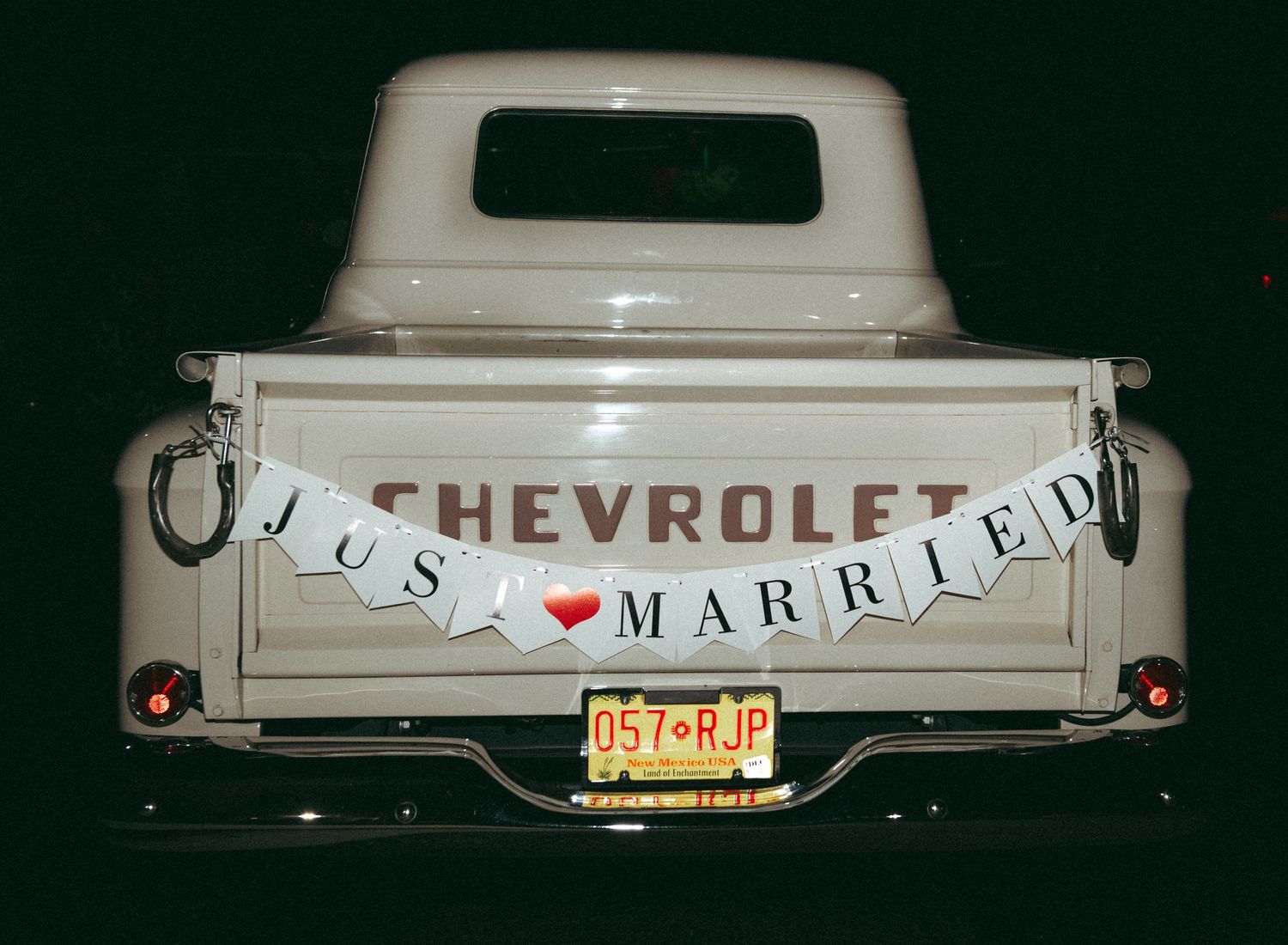 A vintage cream Chevrolet truck displays a Just Married banner at a nighttime wedding celebration.