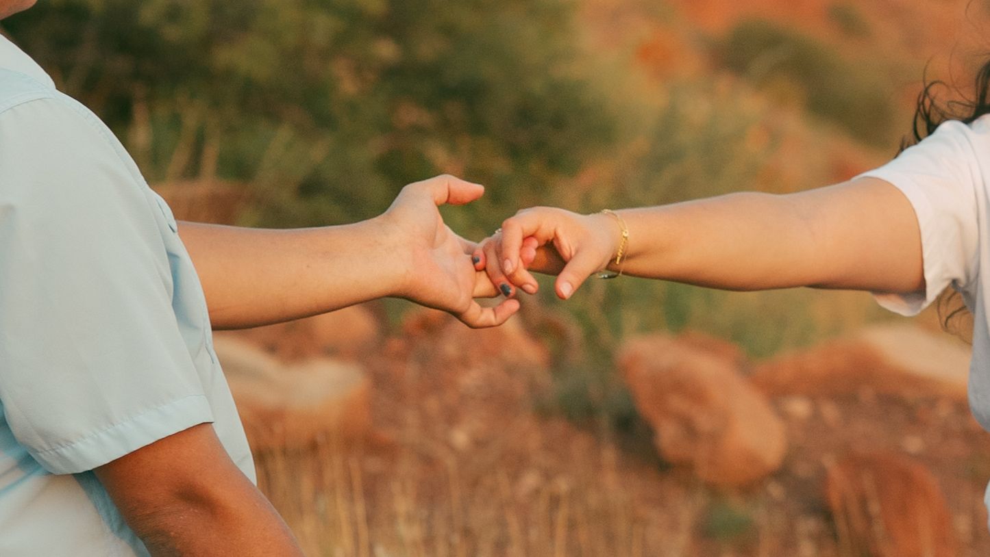 Two people gently holding hands outdoors in a golden field during sunset engagement photo.
