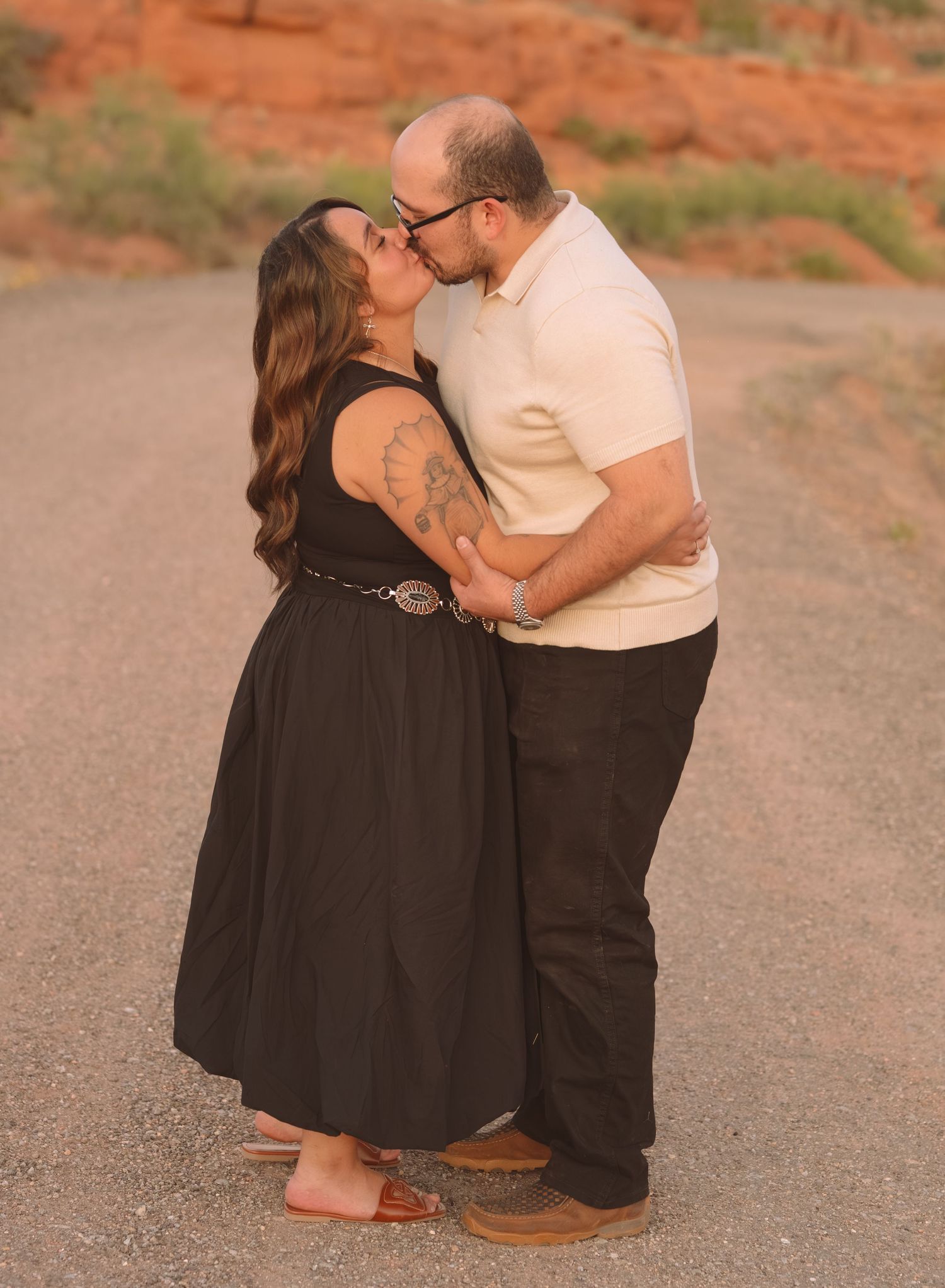 Couple sharing a kiss on a dirt road with red rock formations in the background.