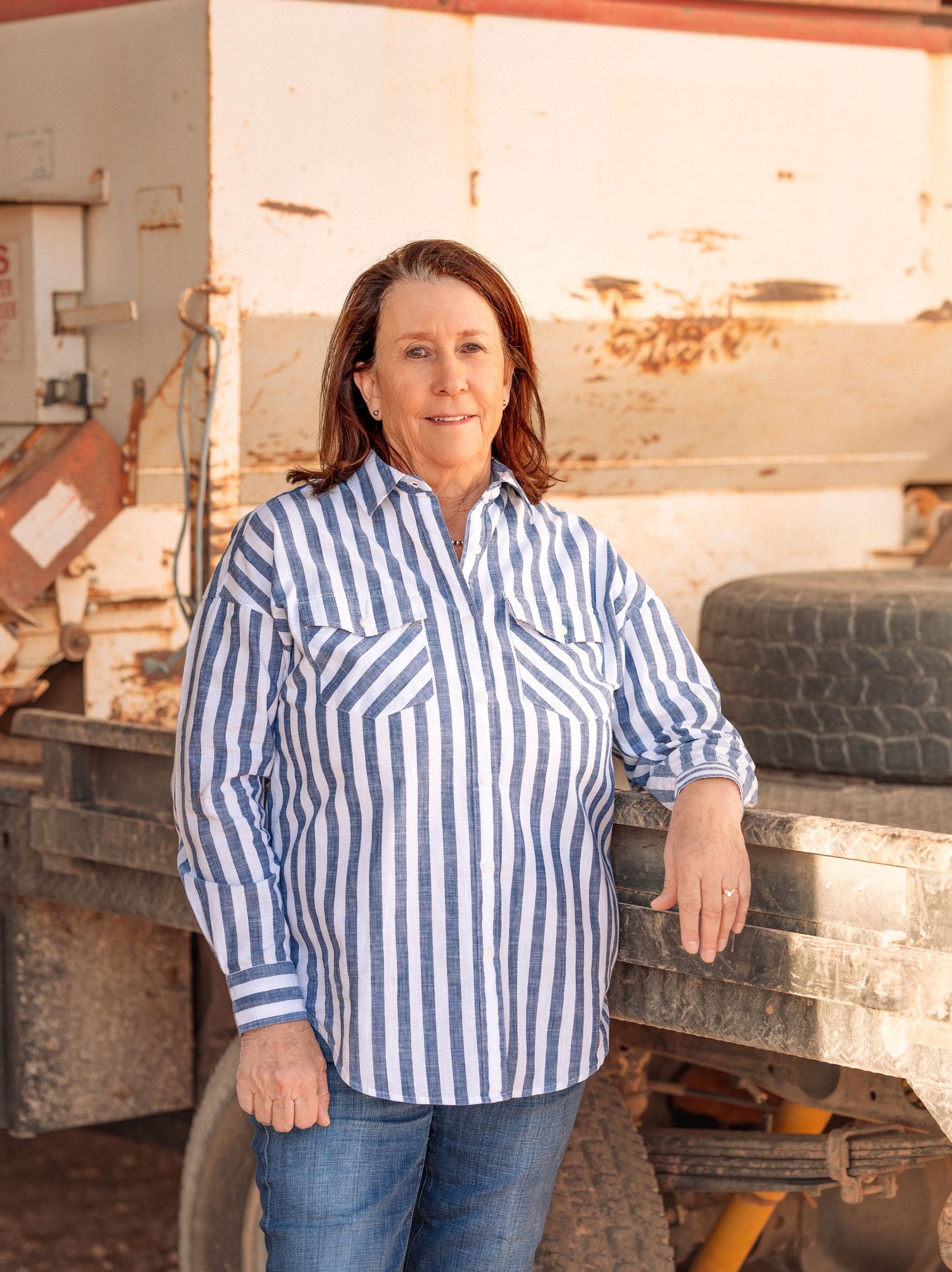 Woman in striped blue shirt leans against rustic farm truck outdoors.