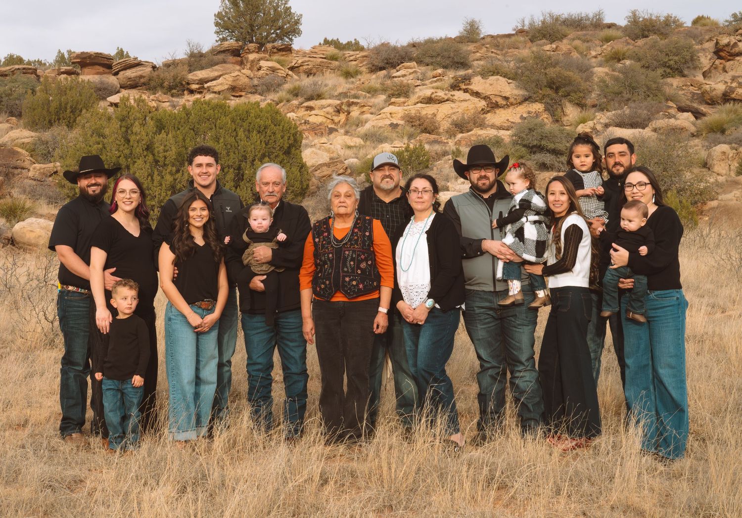 Large extended family group portrait outdoors in desert landscape with rocky hills in background.