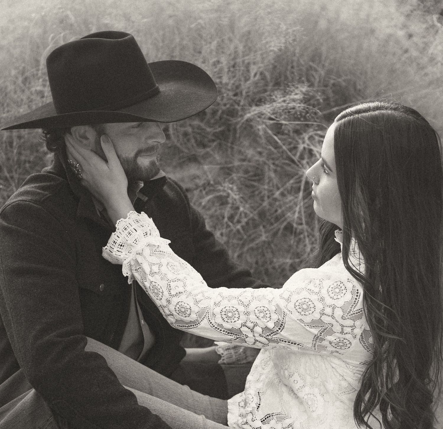 Black and white romantic portrait of couple in western attire, woman tenderly touching man's face.