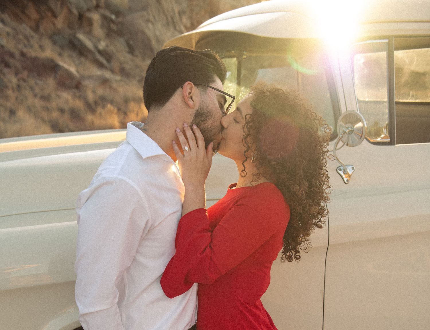 Couple kissing passionately in front of a vintage white van at sunset golden hour.