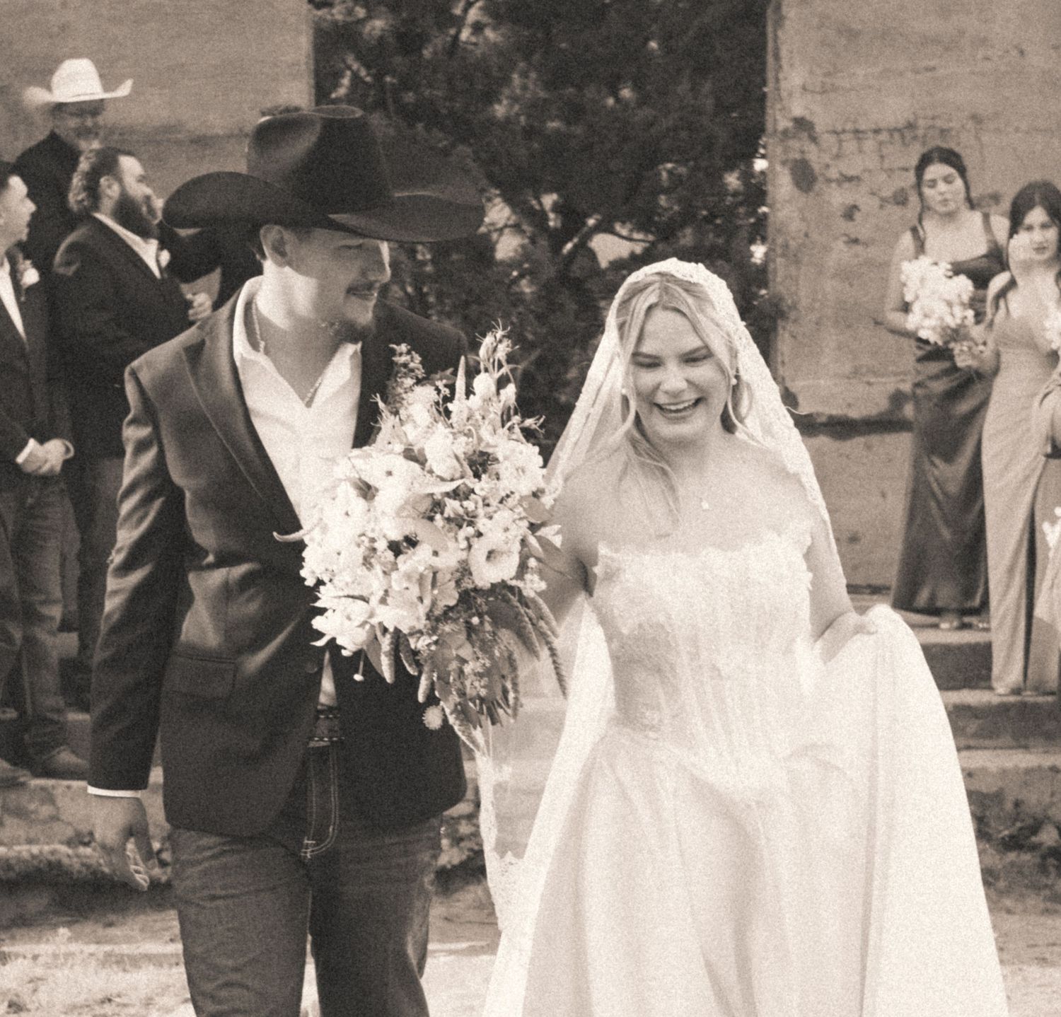 Smiling bride and groom walking back down the aisle after wedding ceremony, groom in cowboy hat.