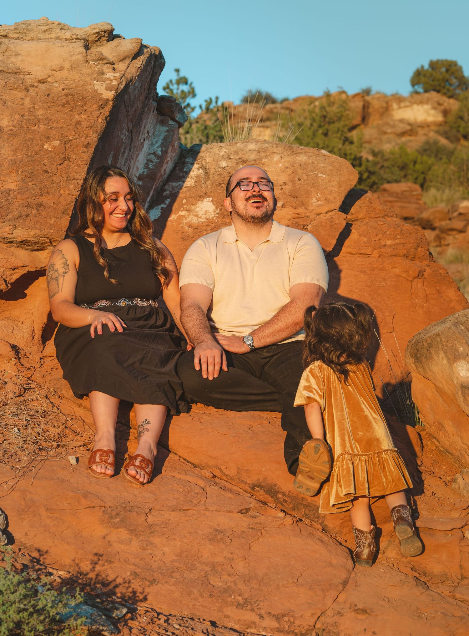 Family of three relaxing on red rocks in warm sunset light in desert setting.