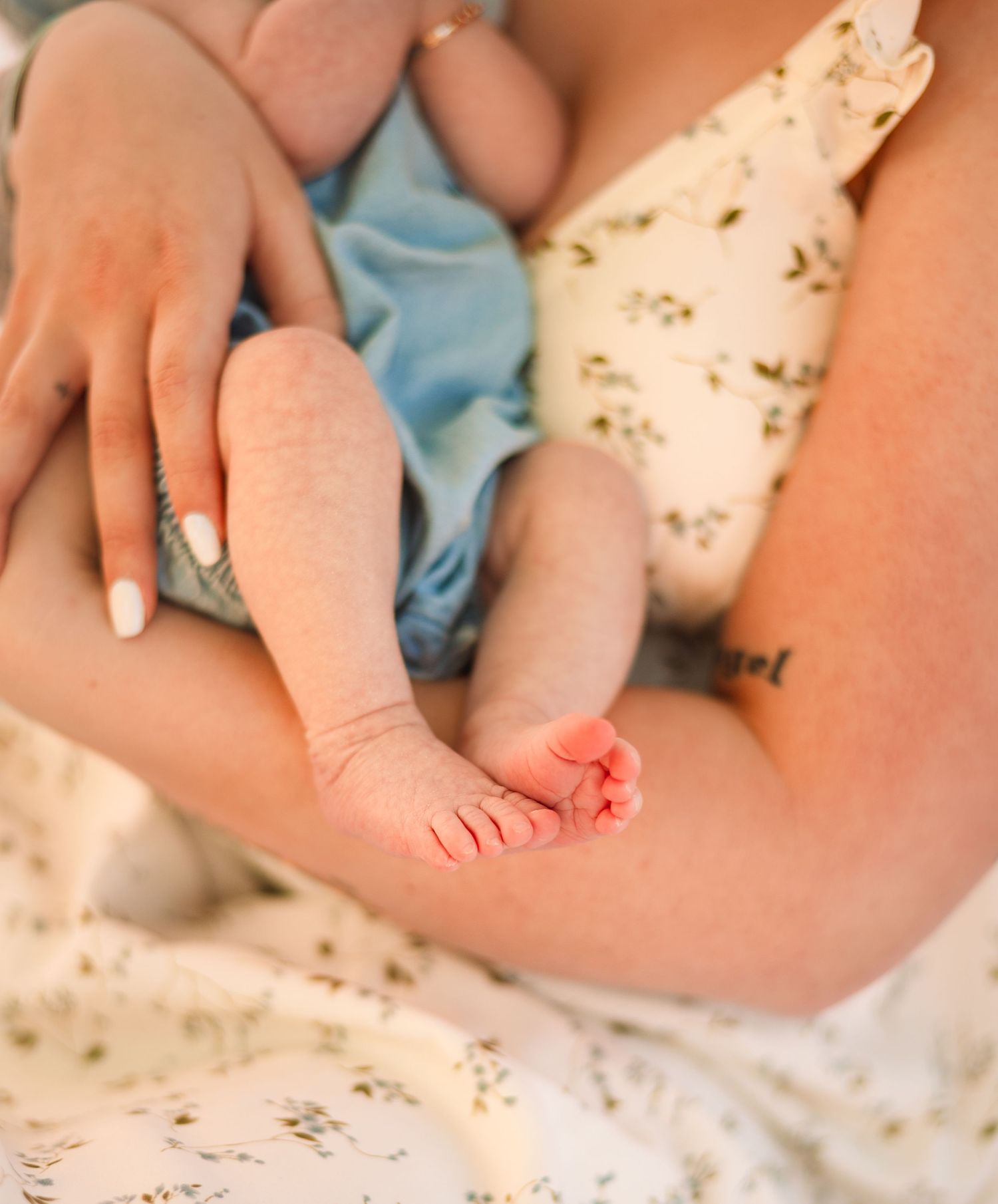 Close-up of a mother in floral dress cradling her newborn baby's tiny feet and legs in her arms.