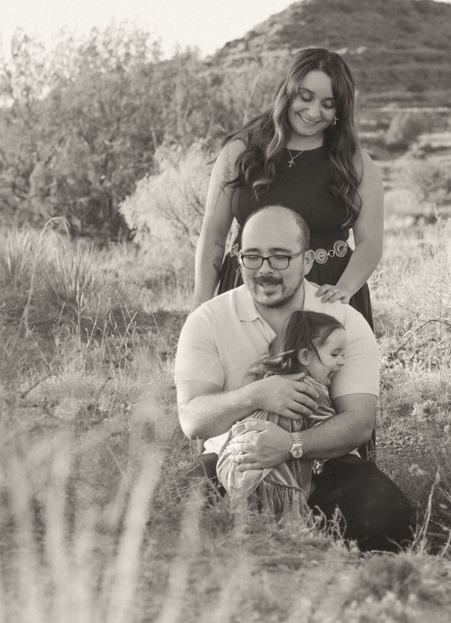 Black and white portrait of couple with baby in natural desert landscape during outdoor family session.