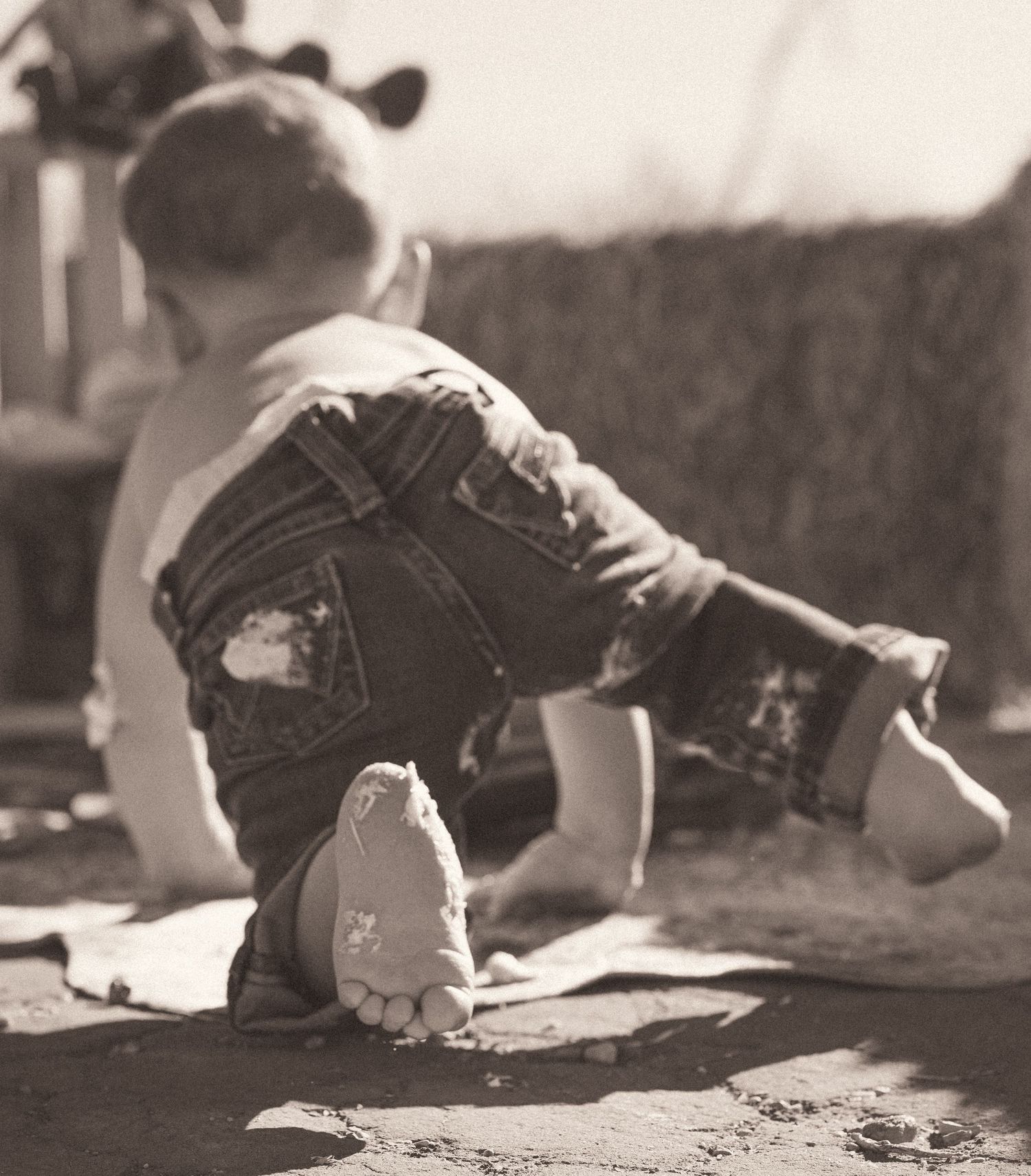 Black and white photo of a toddler in denim overalls crawling outdoors, showing worn shoes and playful exploration.