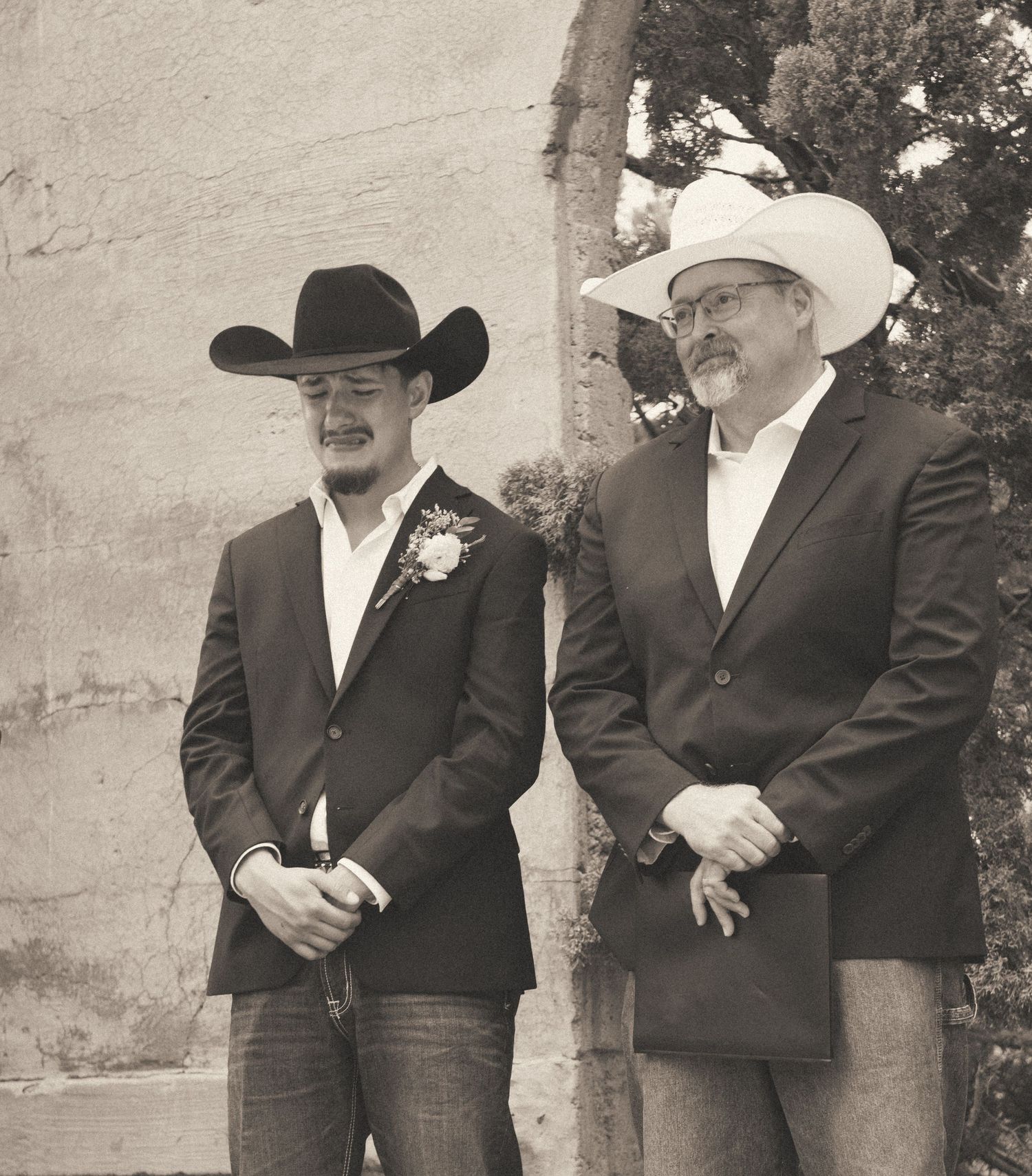 Two men in black suits and cowboy hats standing together at a western-style wedding ceremony.