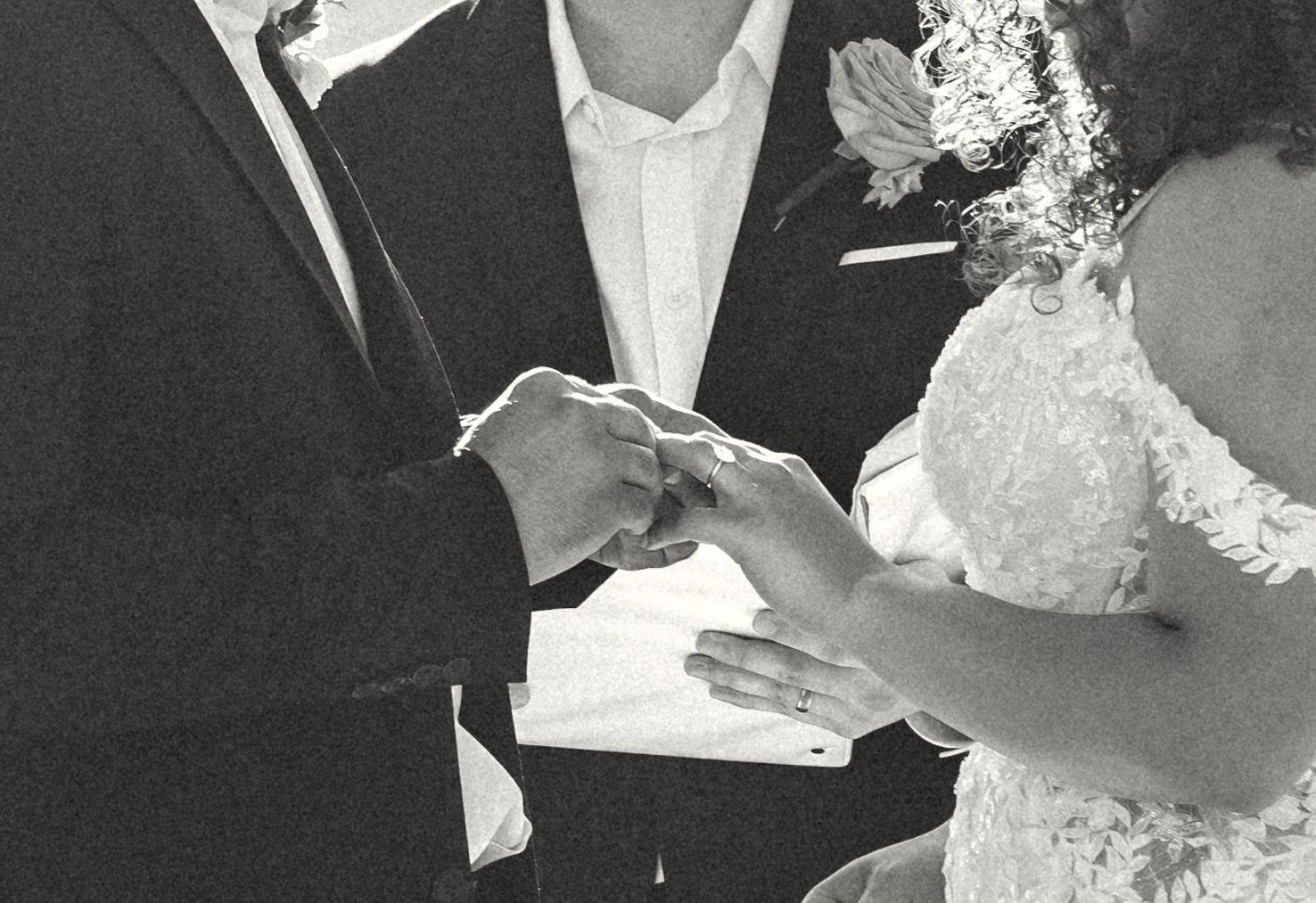 A groom places a wedding ring on the bride's finger during a black and white ceremony close-up.