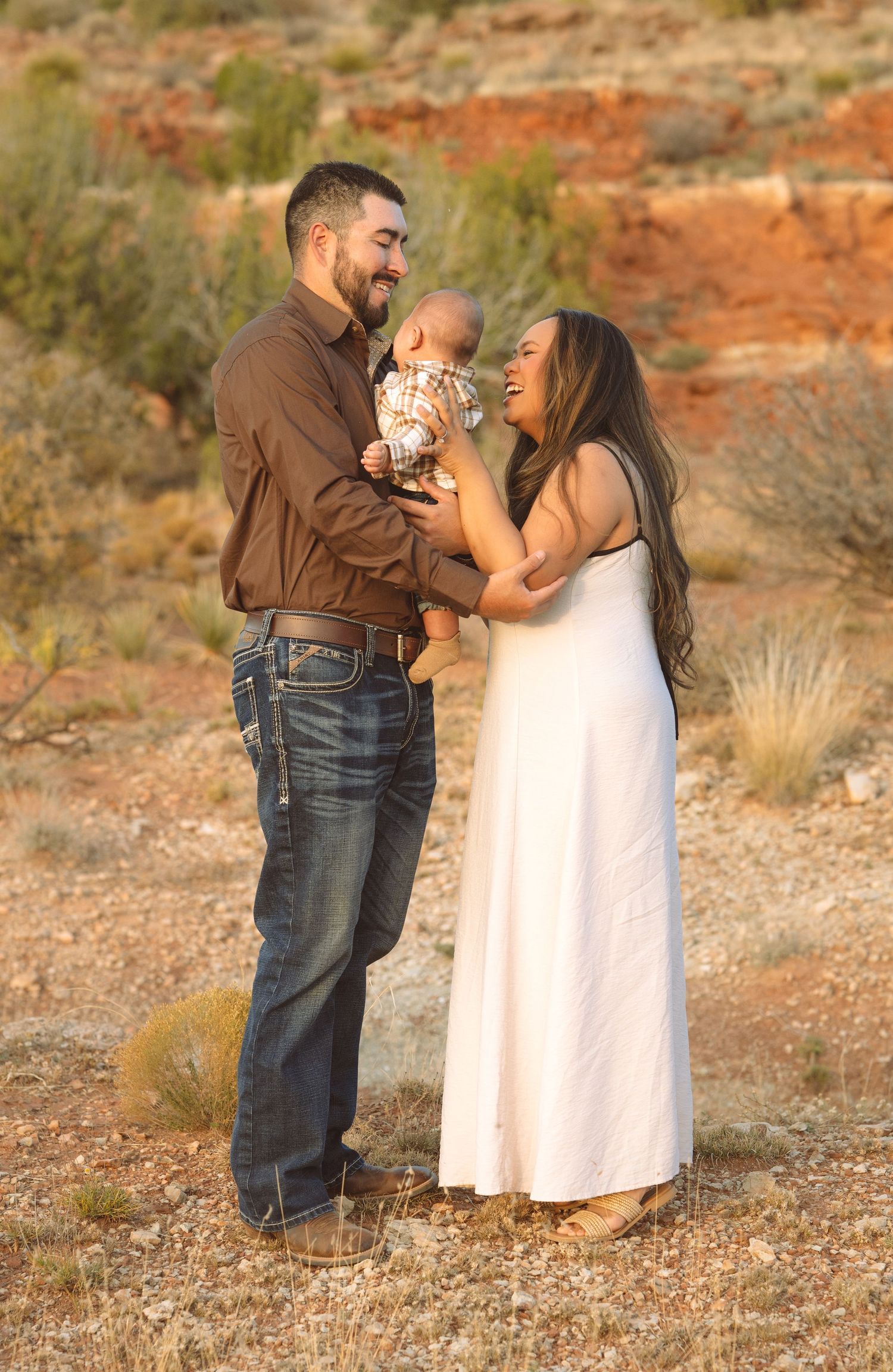 Smiling family with baby in desert landscape at sunset.