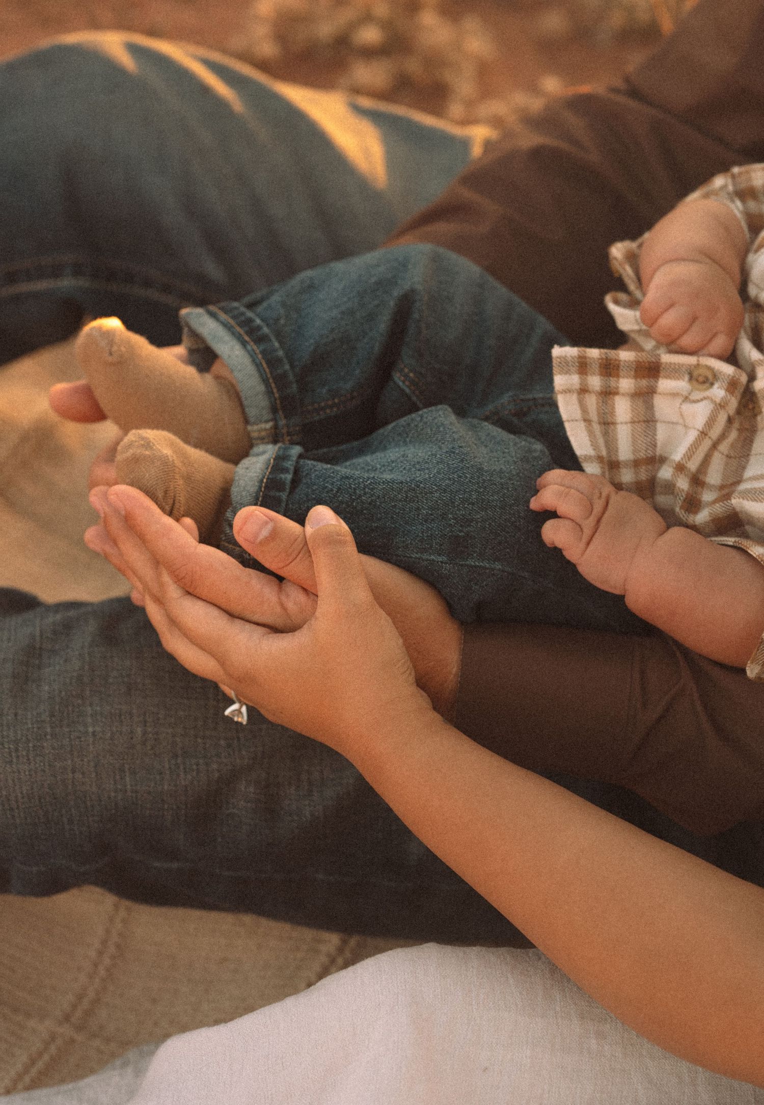 Close-up of parents gently holding a newborn baby's tiny feet and hands on a warm blanket.
