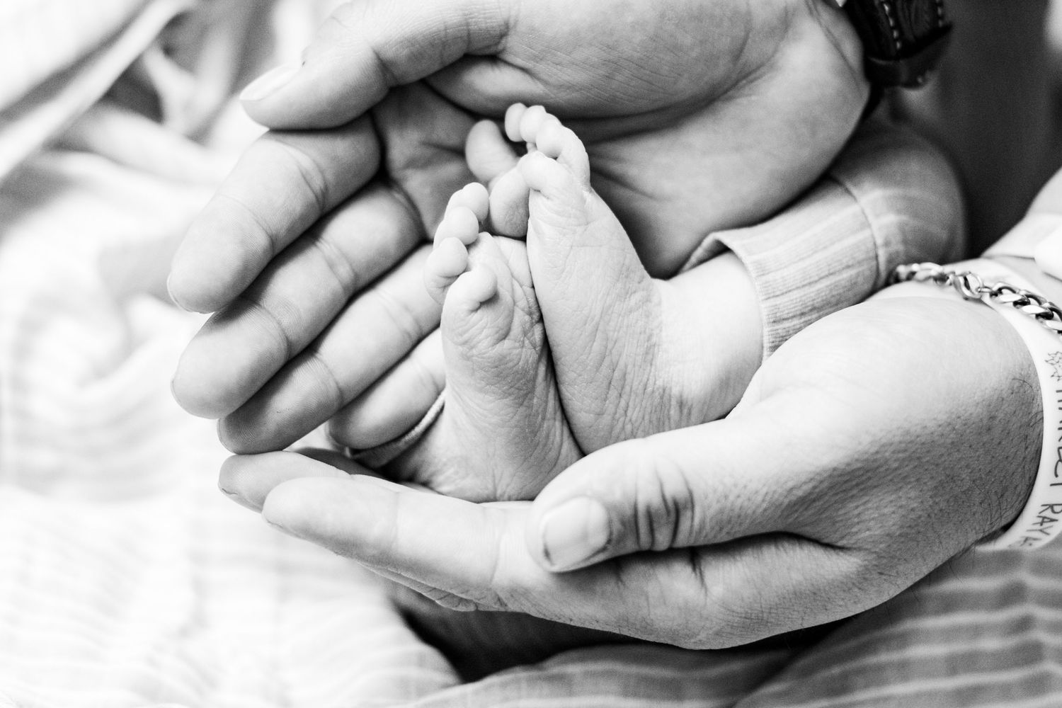 Black and white photo of newborn baby tiny feet cradled in parents hands.