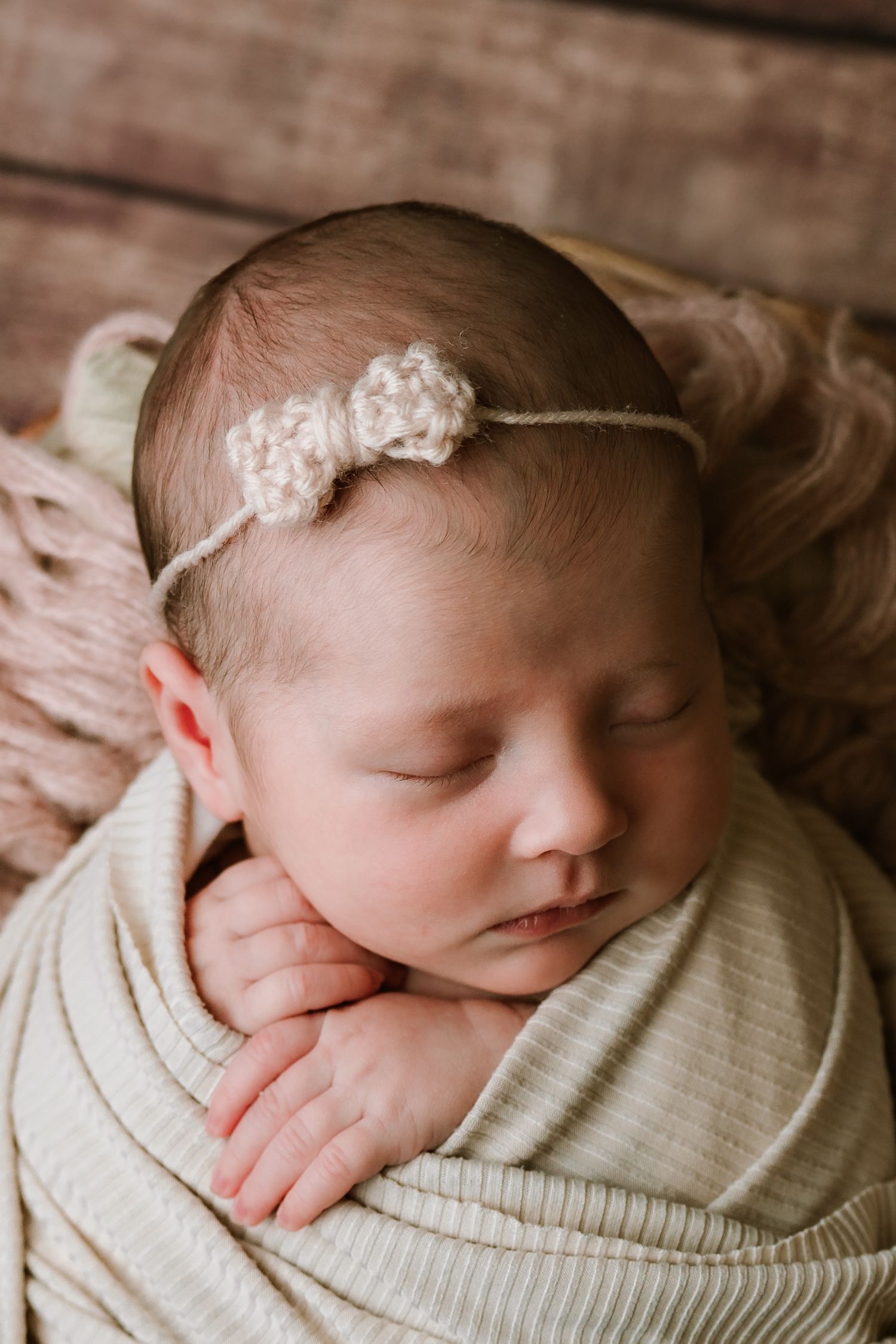 Close-up of sleeping newborn wearing a delicate crochet flower headband in cream wrap.