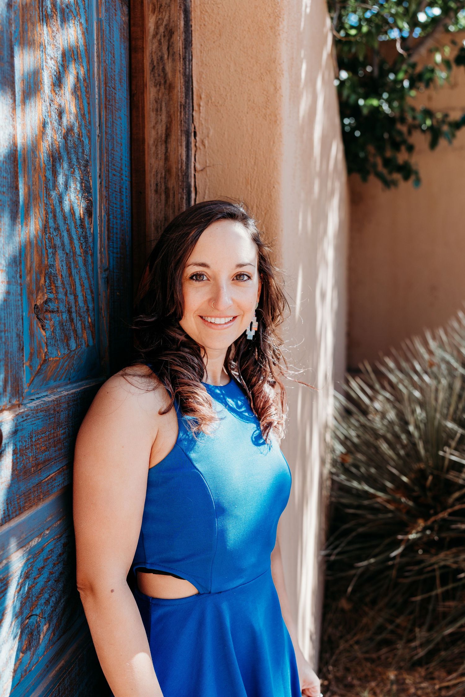Brunette woman in royal blue dress leaning against blue wooden door.