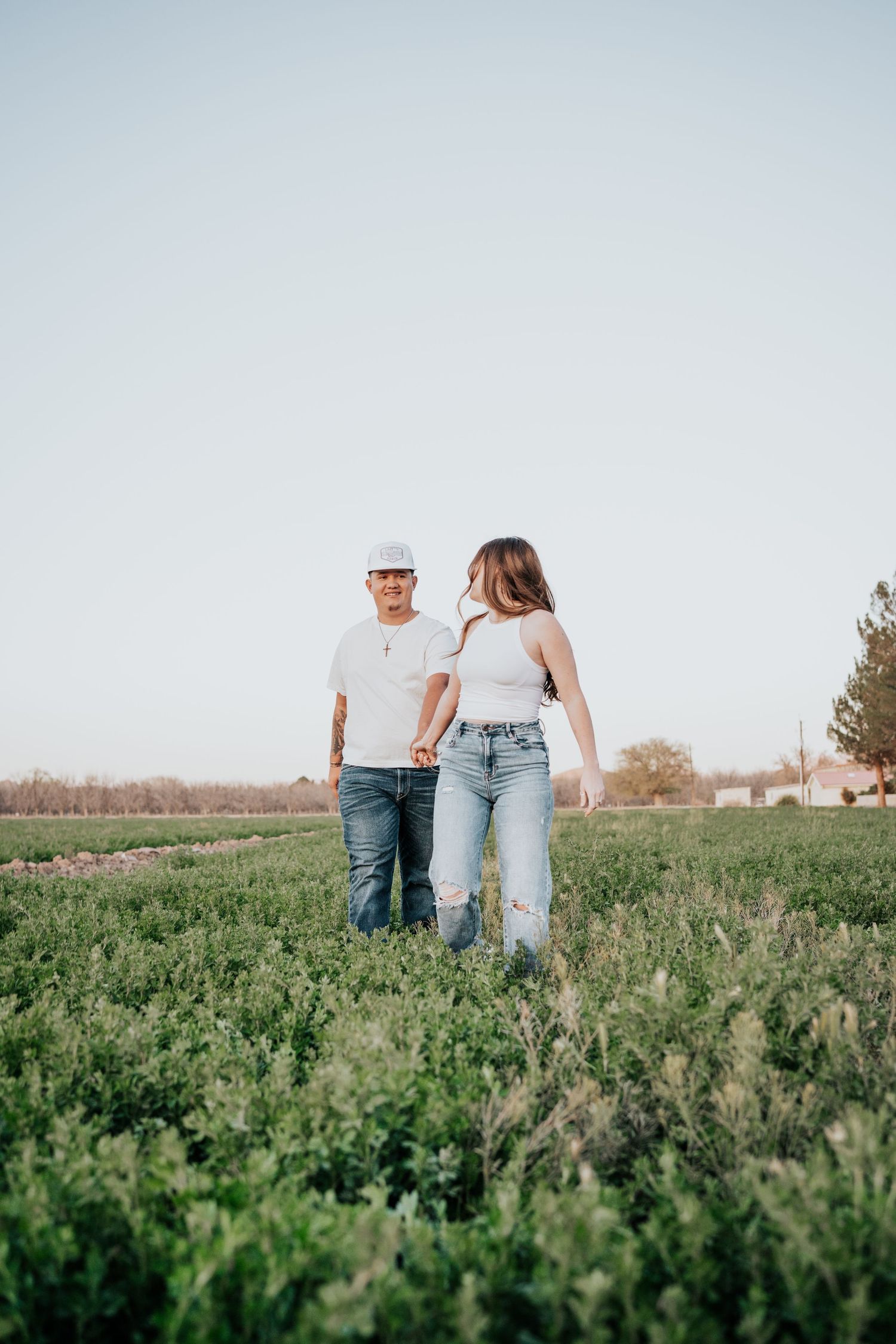 Couple holding hands and walking through a green field during a romantic golden hour photo session.