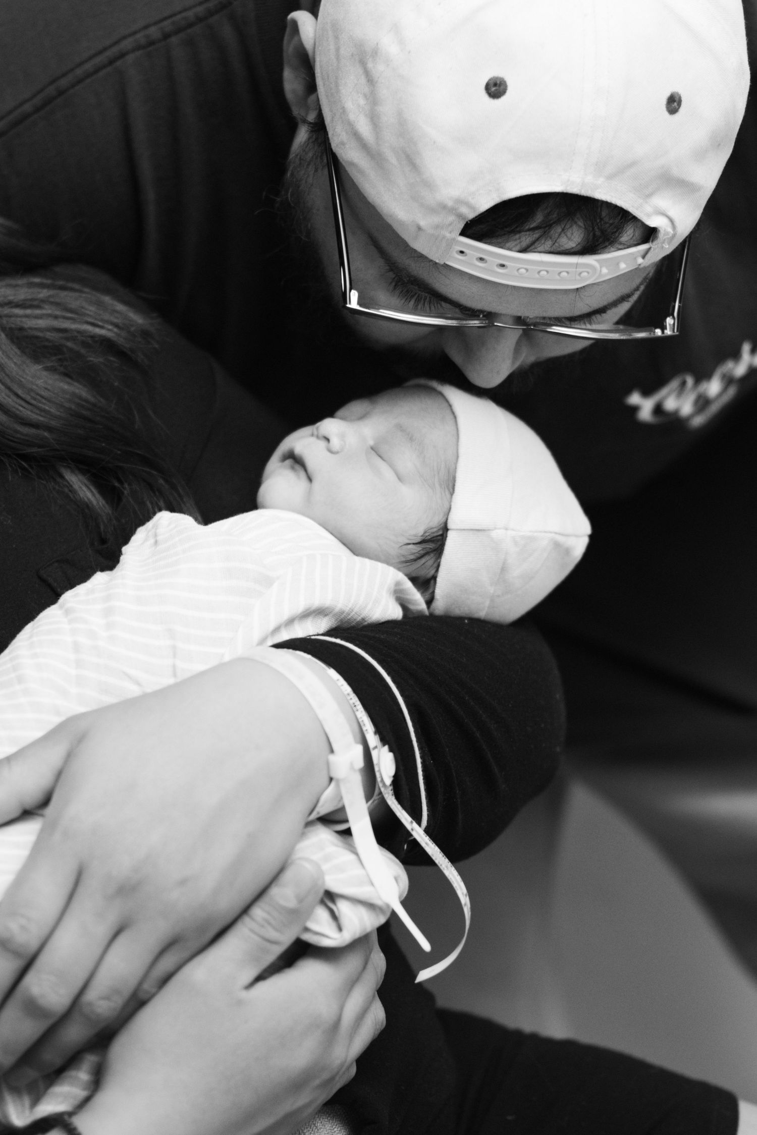 Black and white photo of parents lovingly gazing at their sleeping swaddled newborn baby.