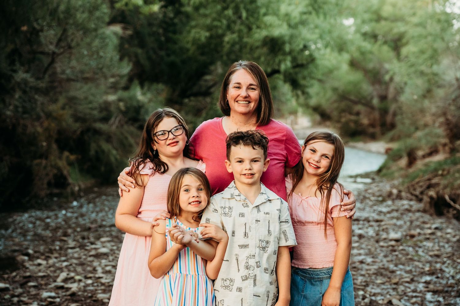 Mom poses with four kids in a warm family portrait by a woodland creek.
