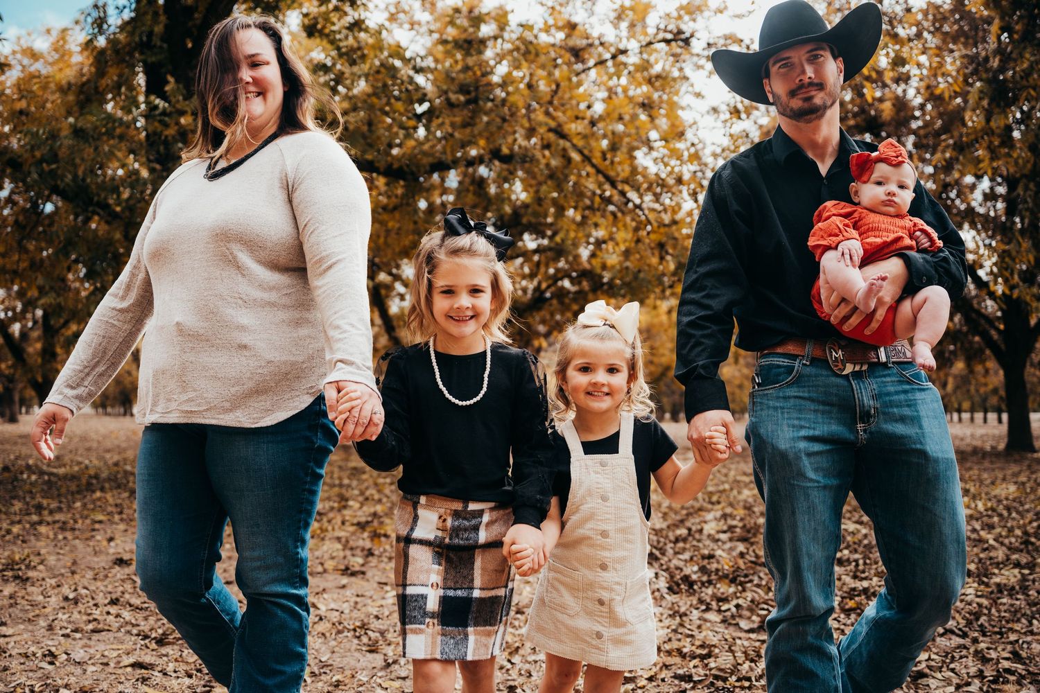 Family of five walking hand-in-hand through golden autumn leaves in park during fall photo session.