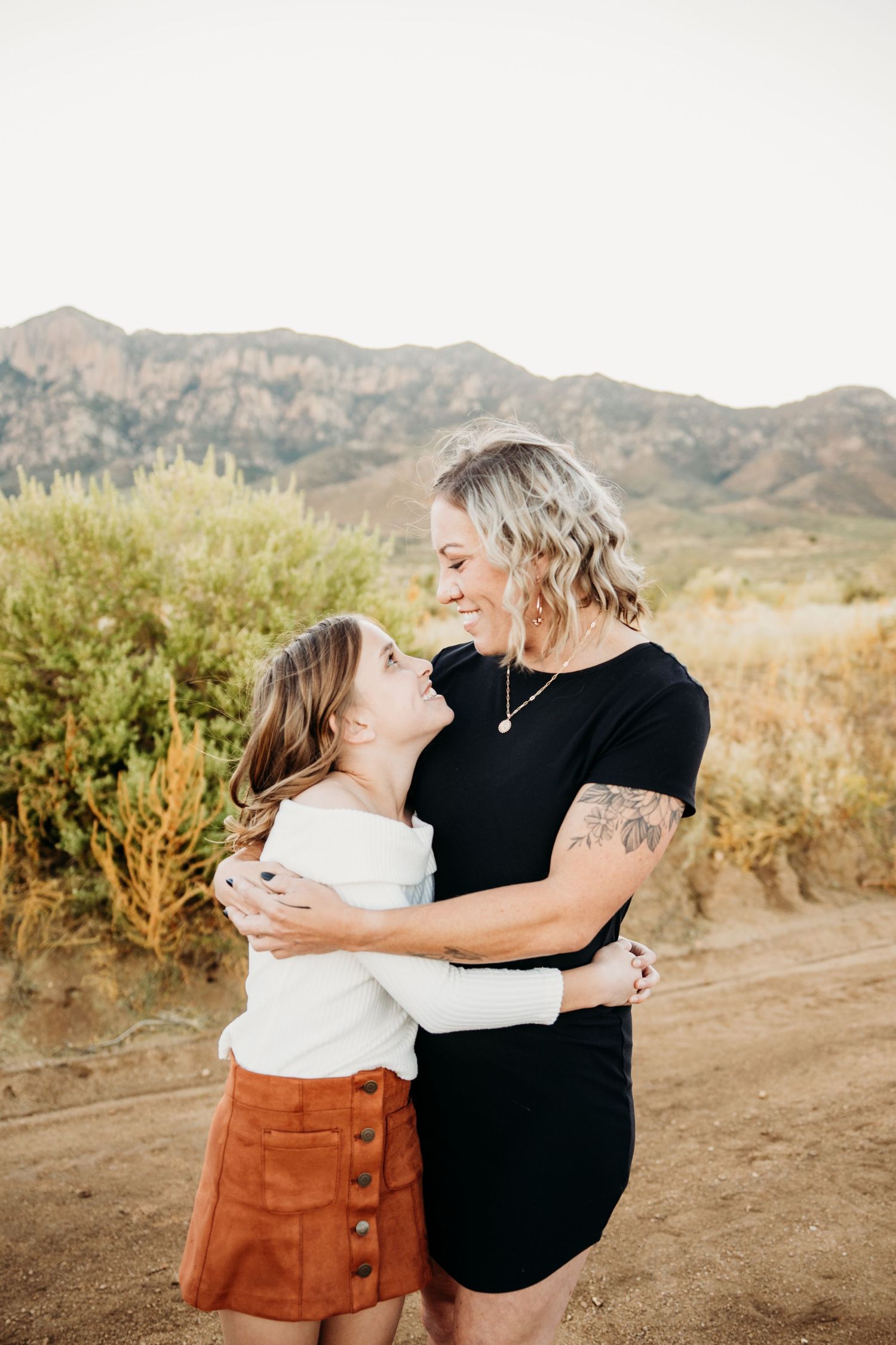 Mother and daughter hugging and smiling at each other in desert setting.