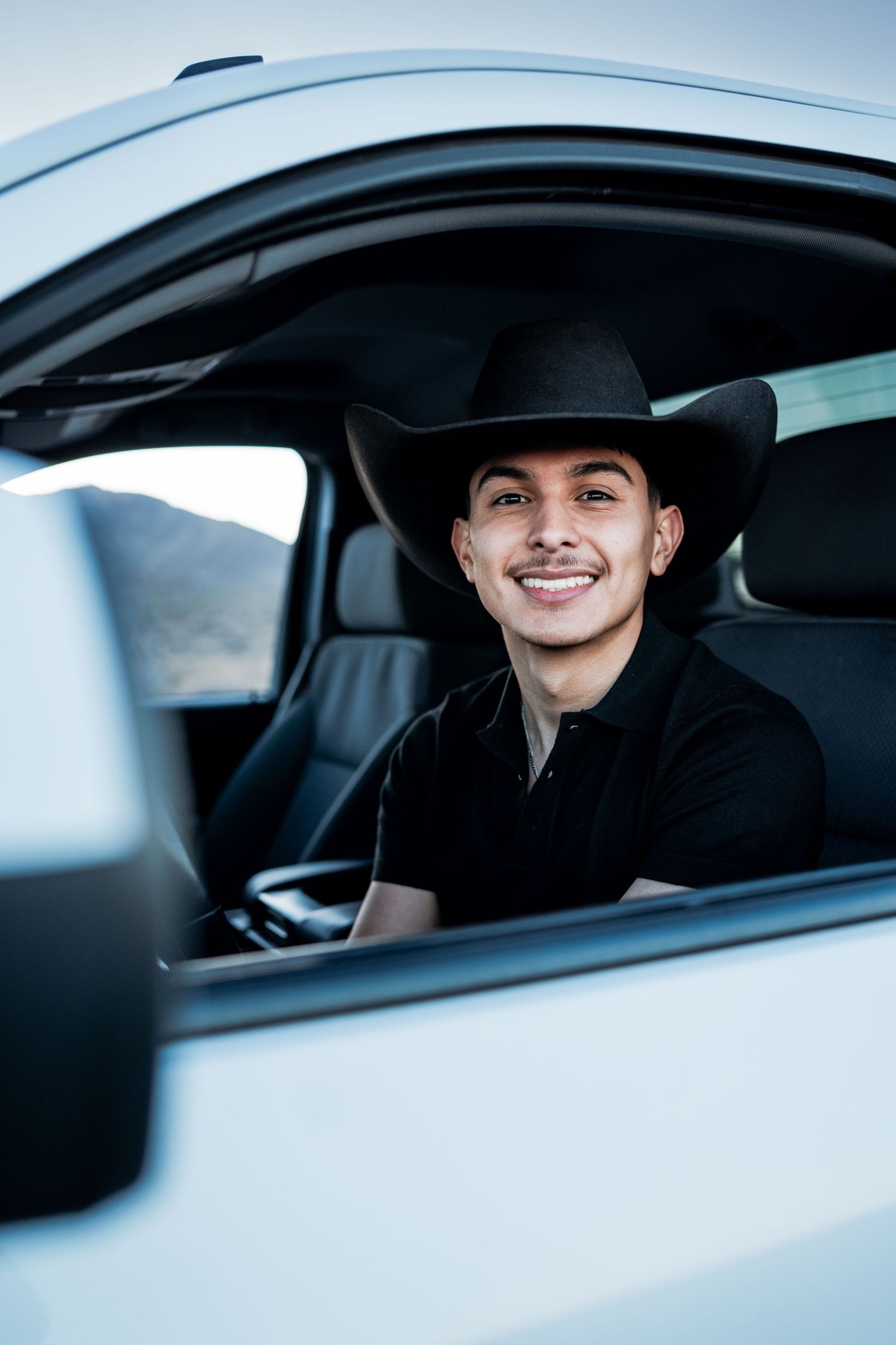 Smiling young man in black cowboy hat sitting in white truck driver seat.