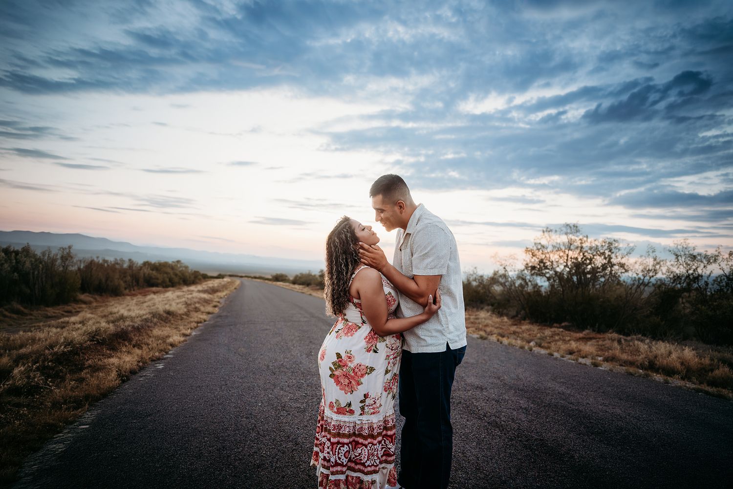 Romantic couple embracing and kissing on a long empty road at dusk with wide open skies.