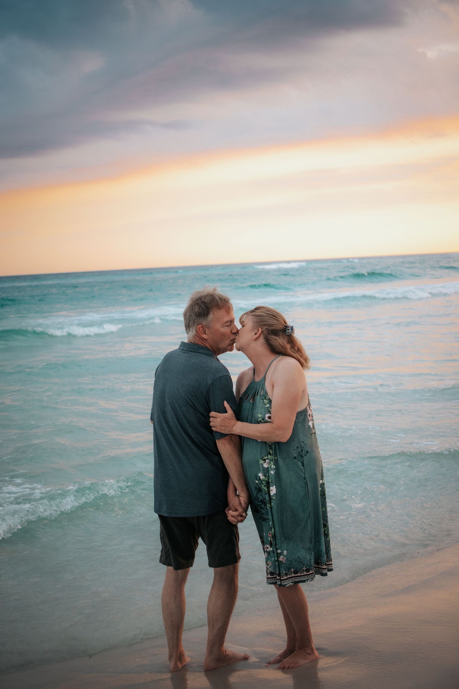 Mature couple sharing a romantic kiss on the beach during a vibrant sunset by the ocean.