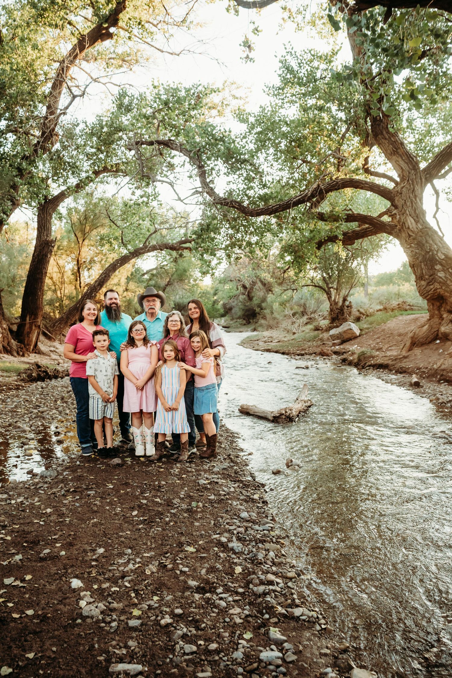 Multi-generational family portrait beside a peaceful creek surrounded by lush trees.