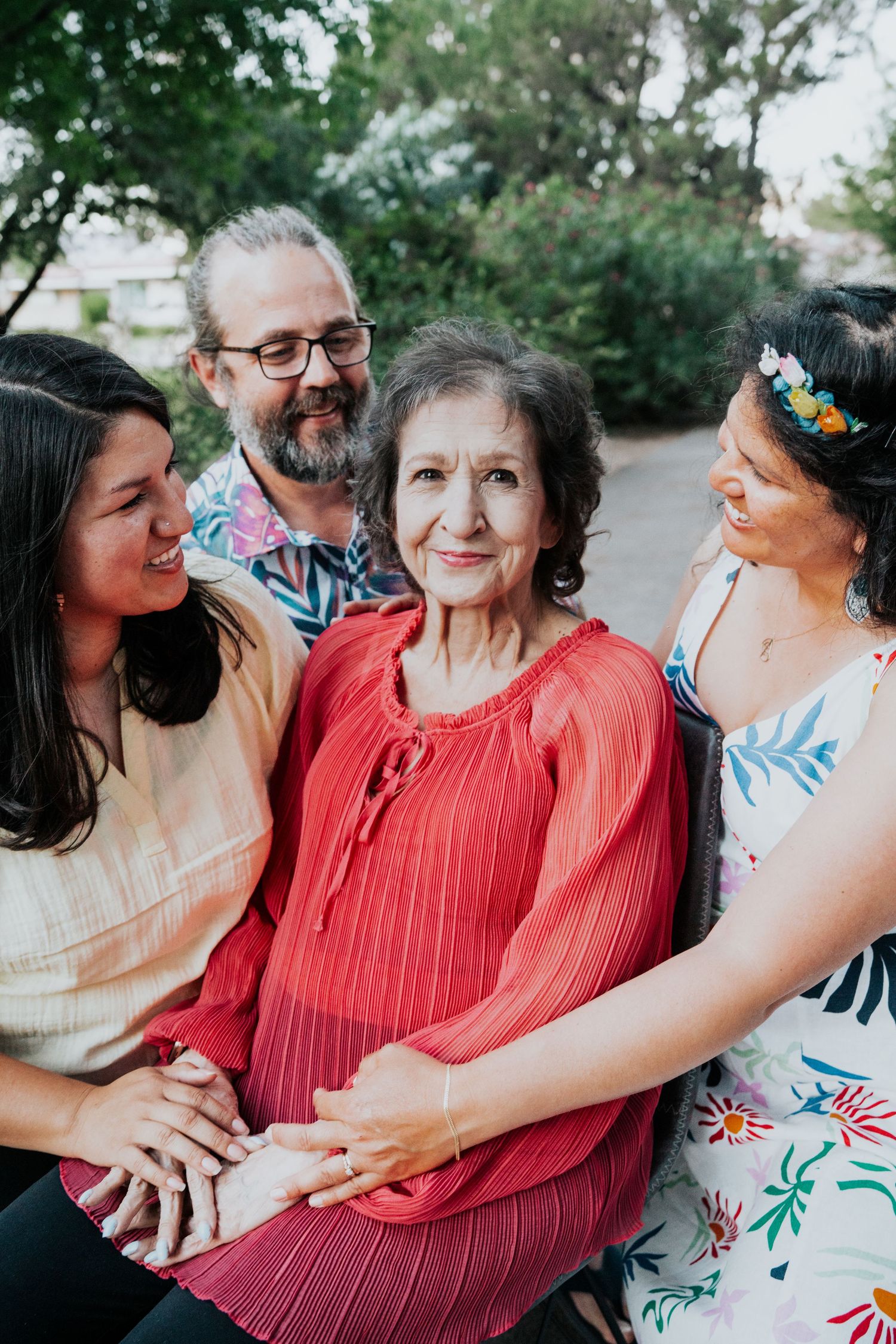 Four family members share a warm moment together outdoors, gathered around a seated elderly woman.