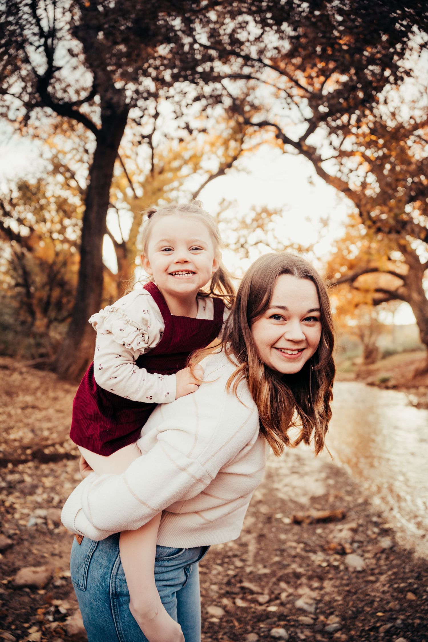 Happy mother and daughter share joyful piggyback moment among fall foliage outdoors.