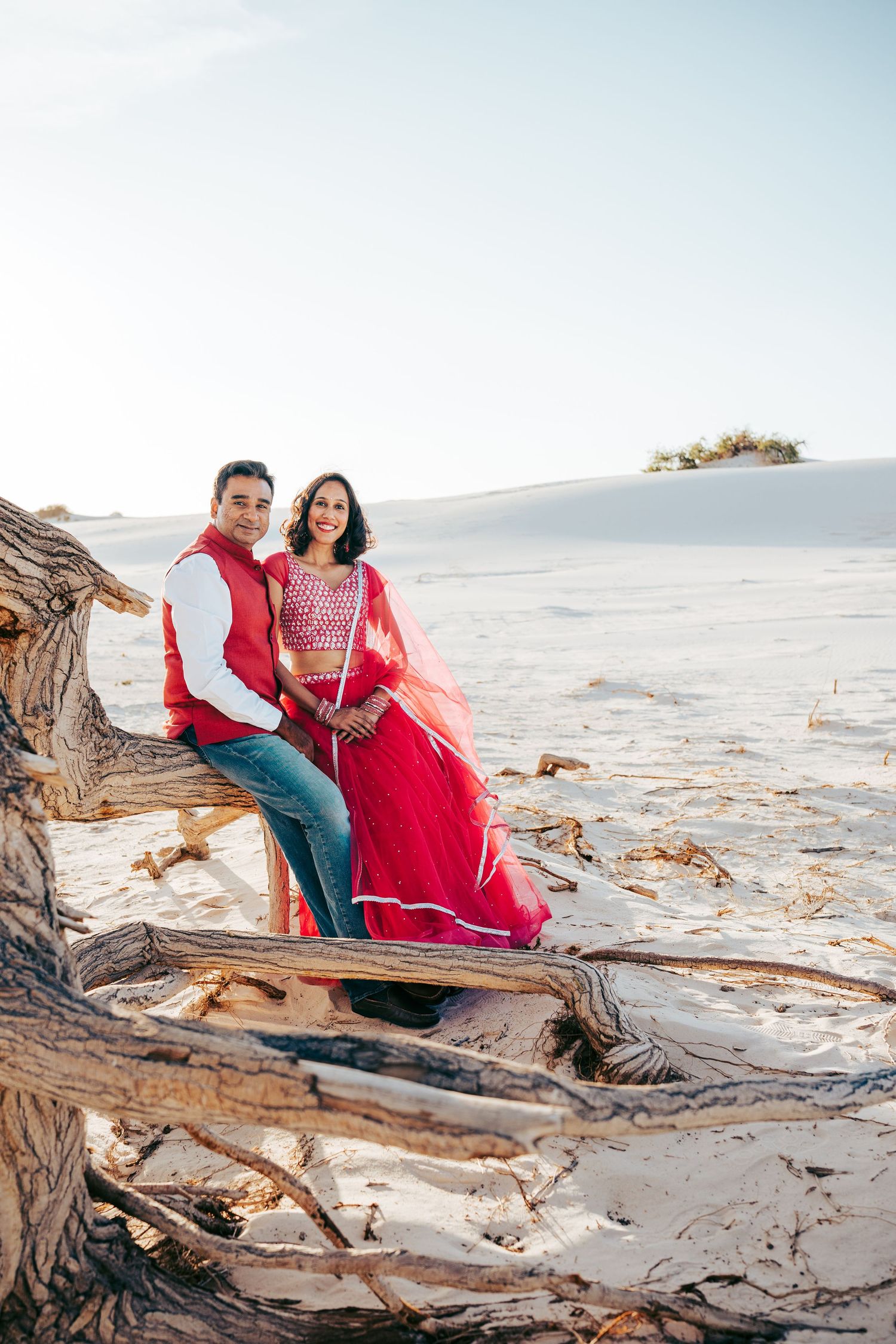 Couple dressed in traditional Indian clothing sitting together on driftwood in a desert landscape.